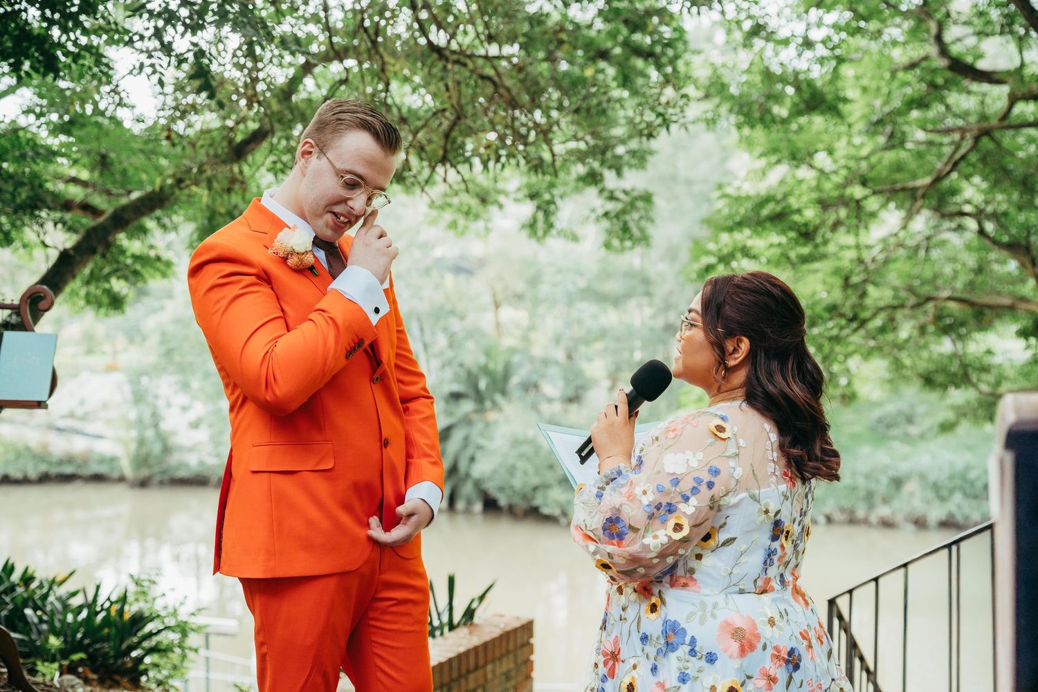 Emotional groom in orange suit listening to speech outdoors at garden wedding.