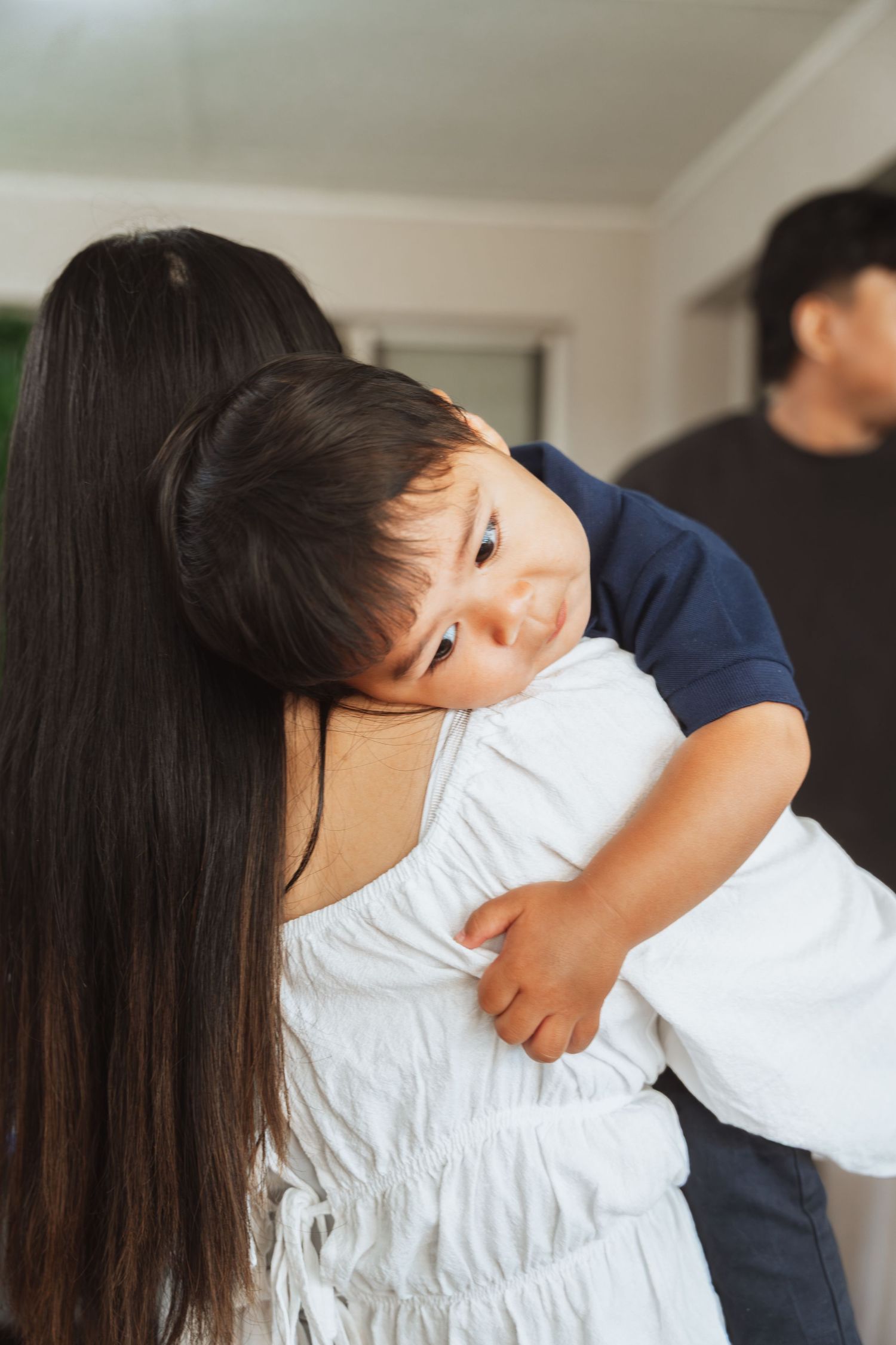 A young child in a navy shirt hugs someone wearing a white dress in a tender family moment at home.