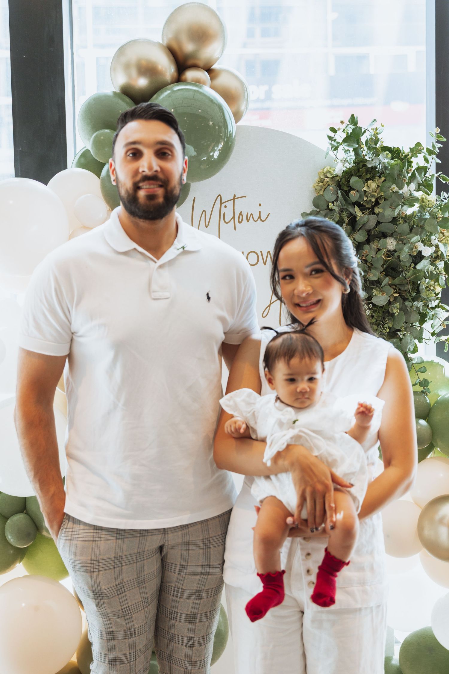 Family wearing coordinated white shirts and plaid pants pose together at a celebration with balloon decorations.