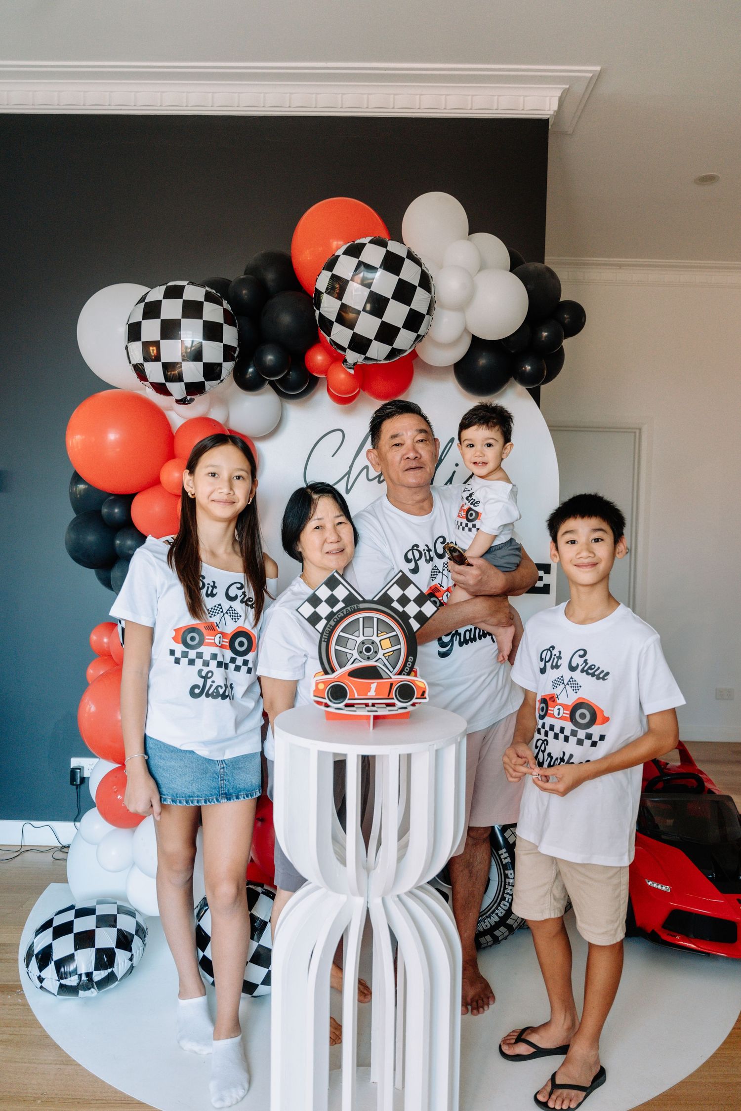 Family gathering with matching white t-shirts and checkered decorations featuring black, white and orange balloons.
