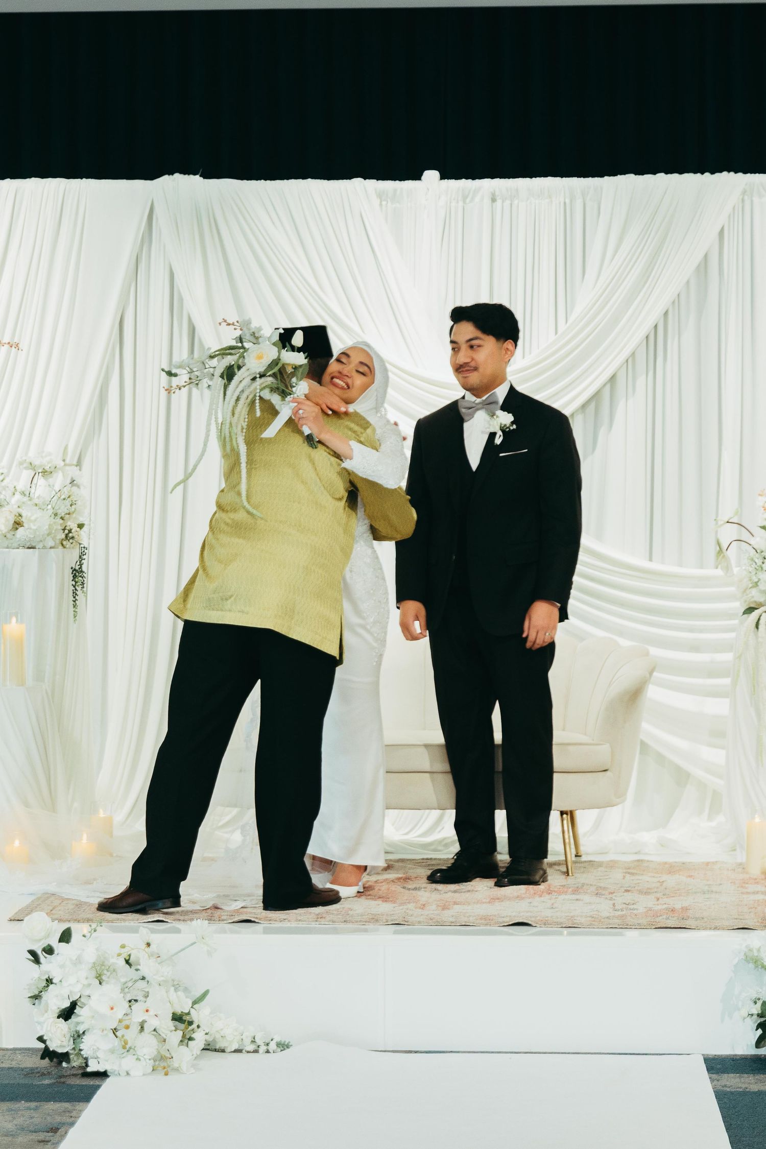 Guest taking selfie with groom in black suit at elegant white draped wedding reception.