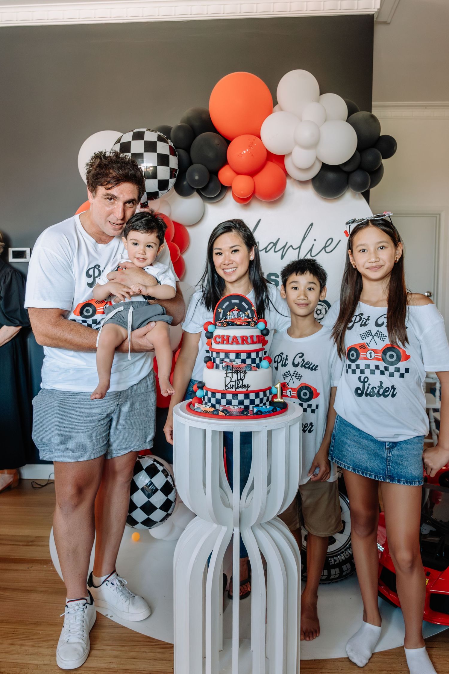 Racing themed birthday party with balloon arch in orange, black and white checkered pattern decorations.