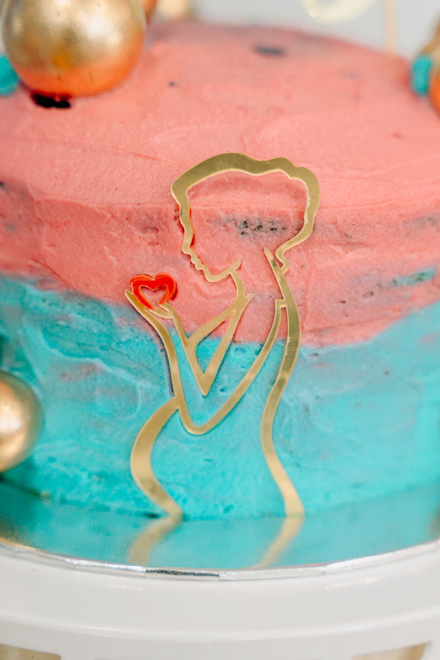 Close-up of a coral pink and turquoise blue cake with gold metallic decorative elements on top.