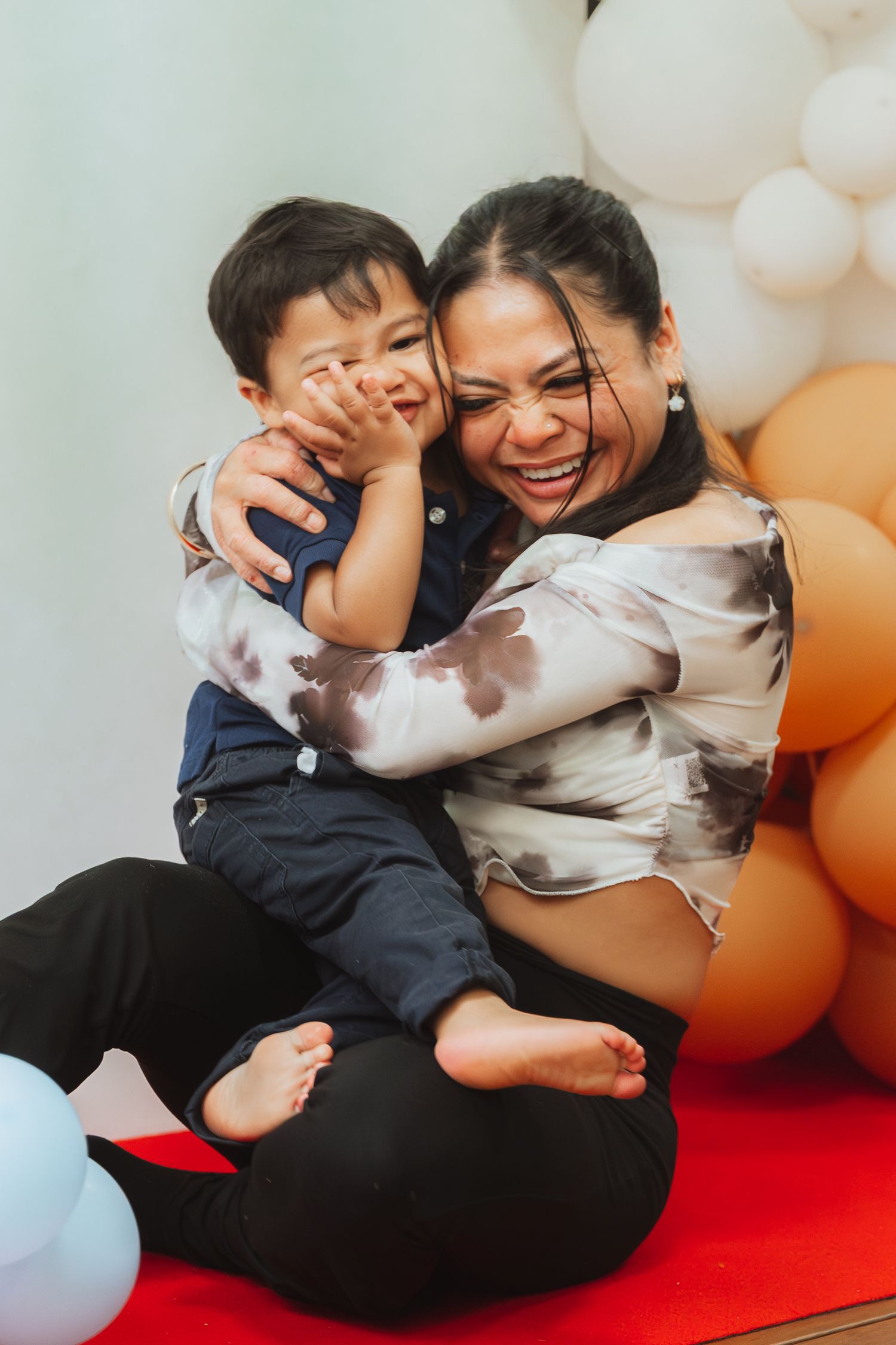A joyful moment of playful interaction on a red mat with white and orange balloons in the background.