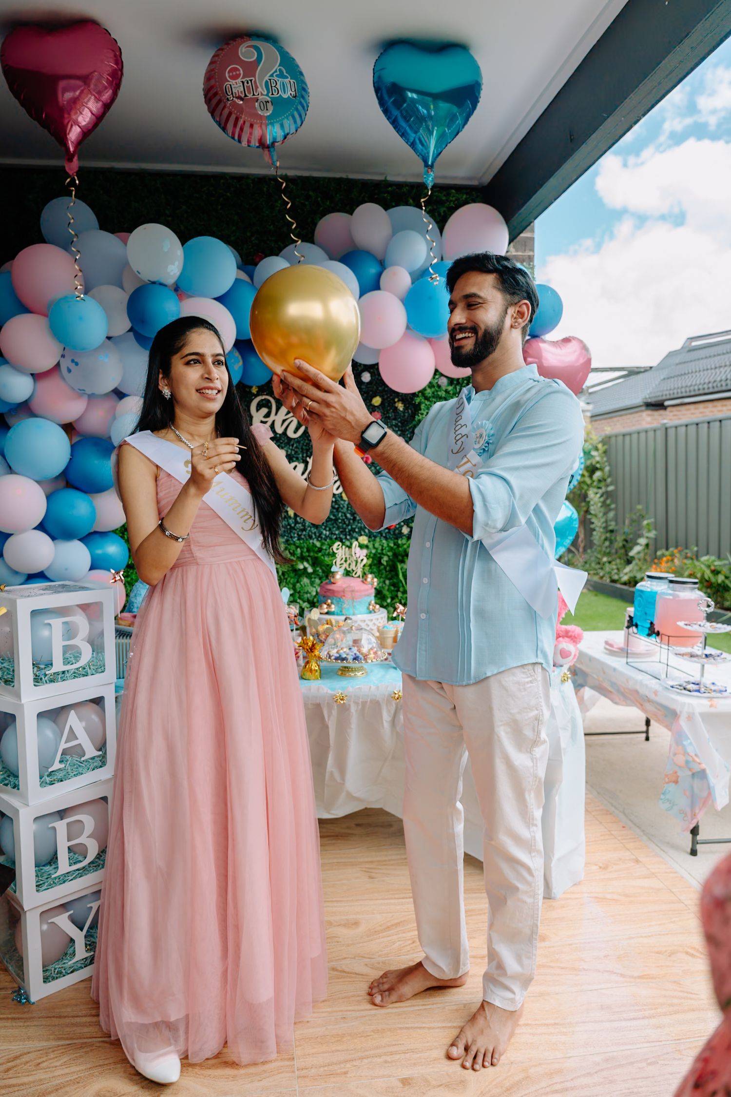 Gender reveal party setup with pink and blue balloon decorations and people celebrating.
