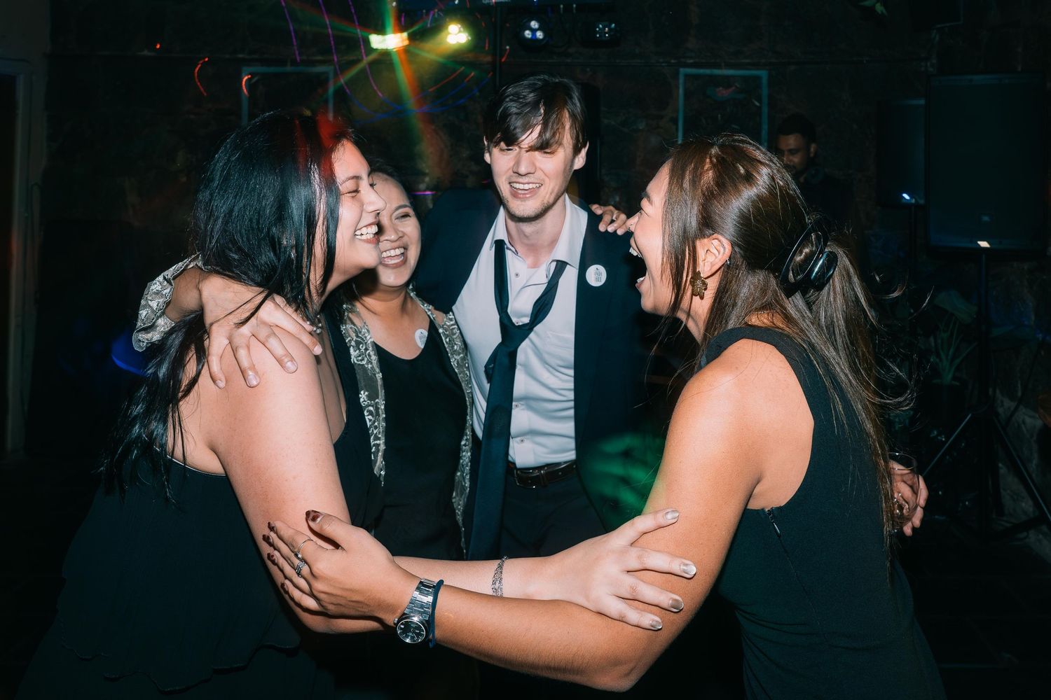 Group of friends laughing and dancing together at a nightclub party with colorful lights.