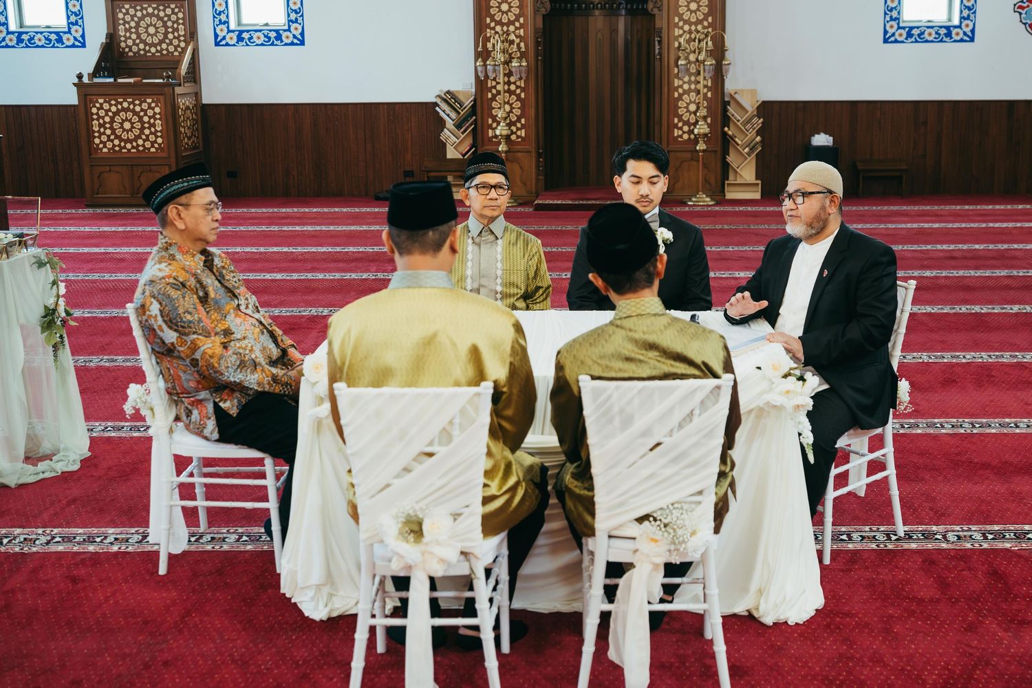 Muslim men in traditional attire gathered around a table in a mosque for an Islamic wedding ceremony.