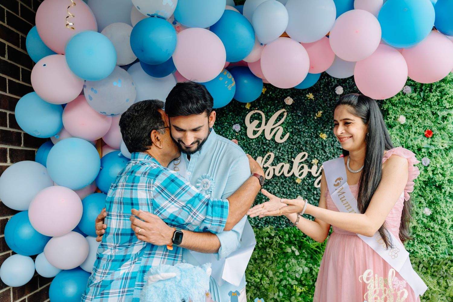 Pink and blue balloon arch decoration against a brick wall with greenery.