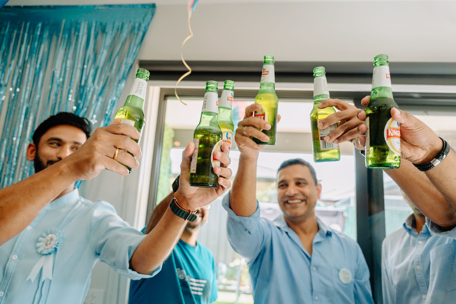 Friends raising bottles in celebration toast with turquoise decorations in background.