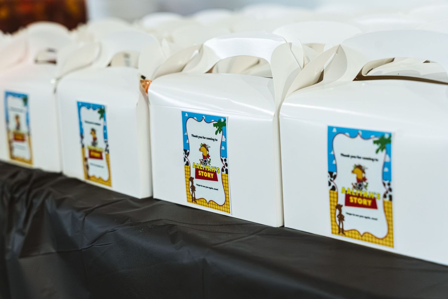 Row of white cardboard favor boxes with decorative blue labels lined up on a dark surface.