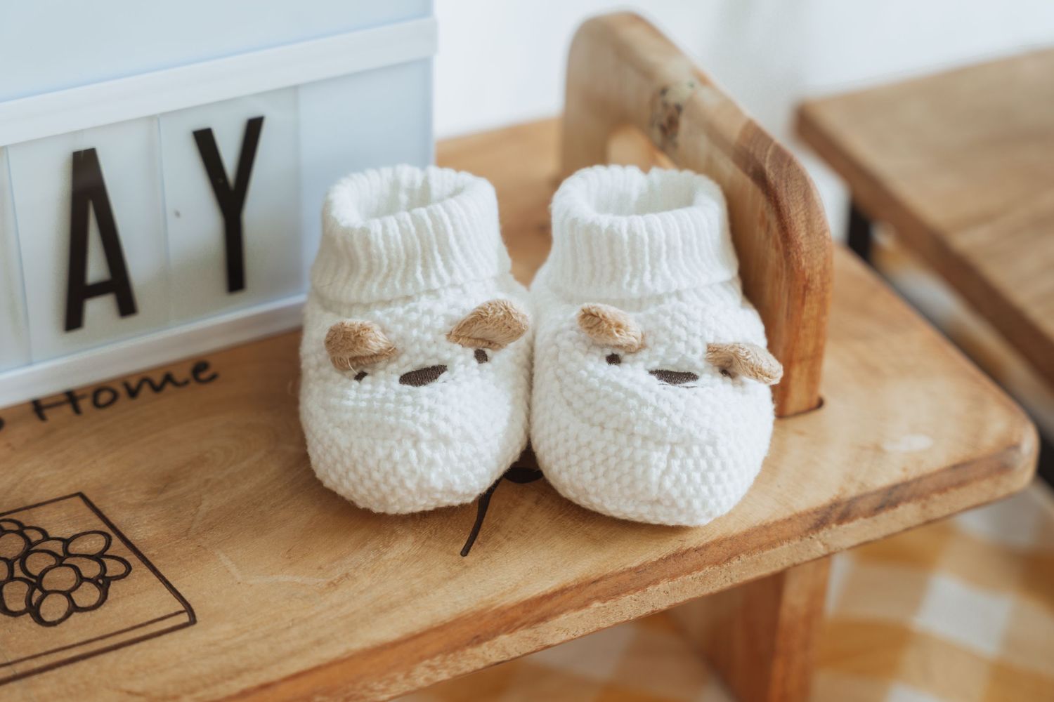 Handmade white crochet baby booties with delicate bow details displayed on a rustic wooden surface.