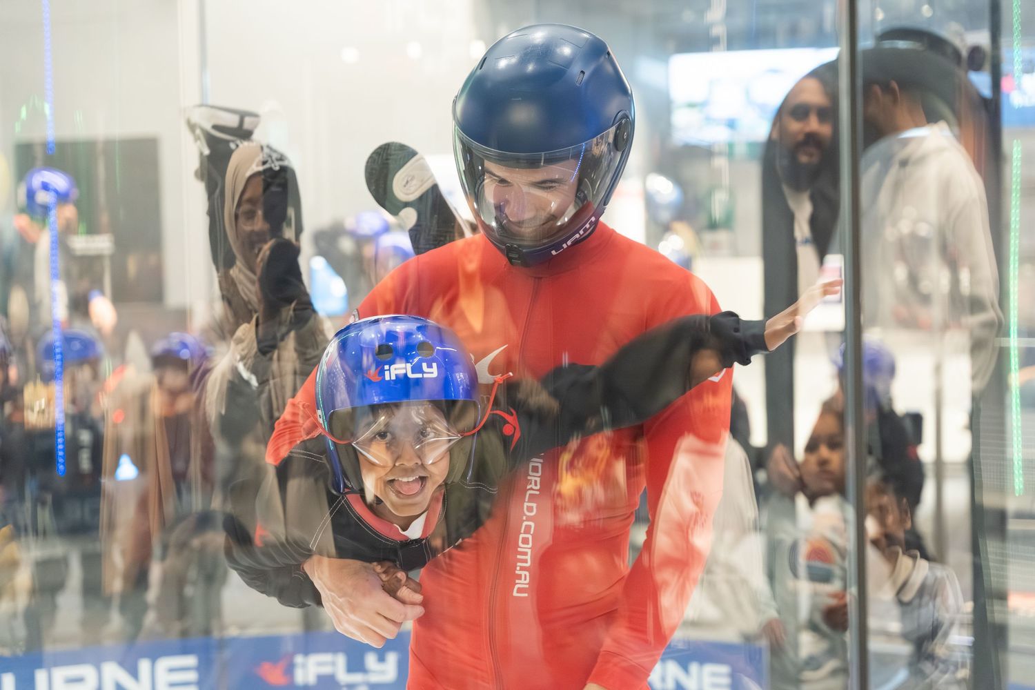 Two people in protective gear and helmets enjoying indoor skydiving at a vertical wind tunnel facility.