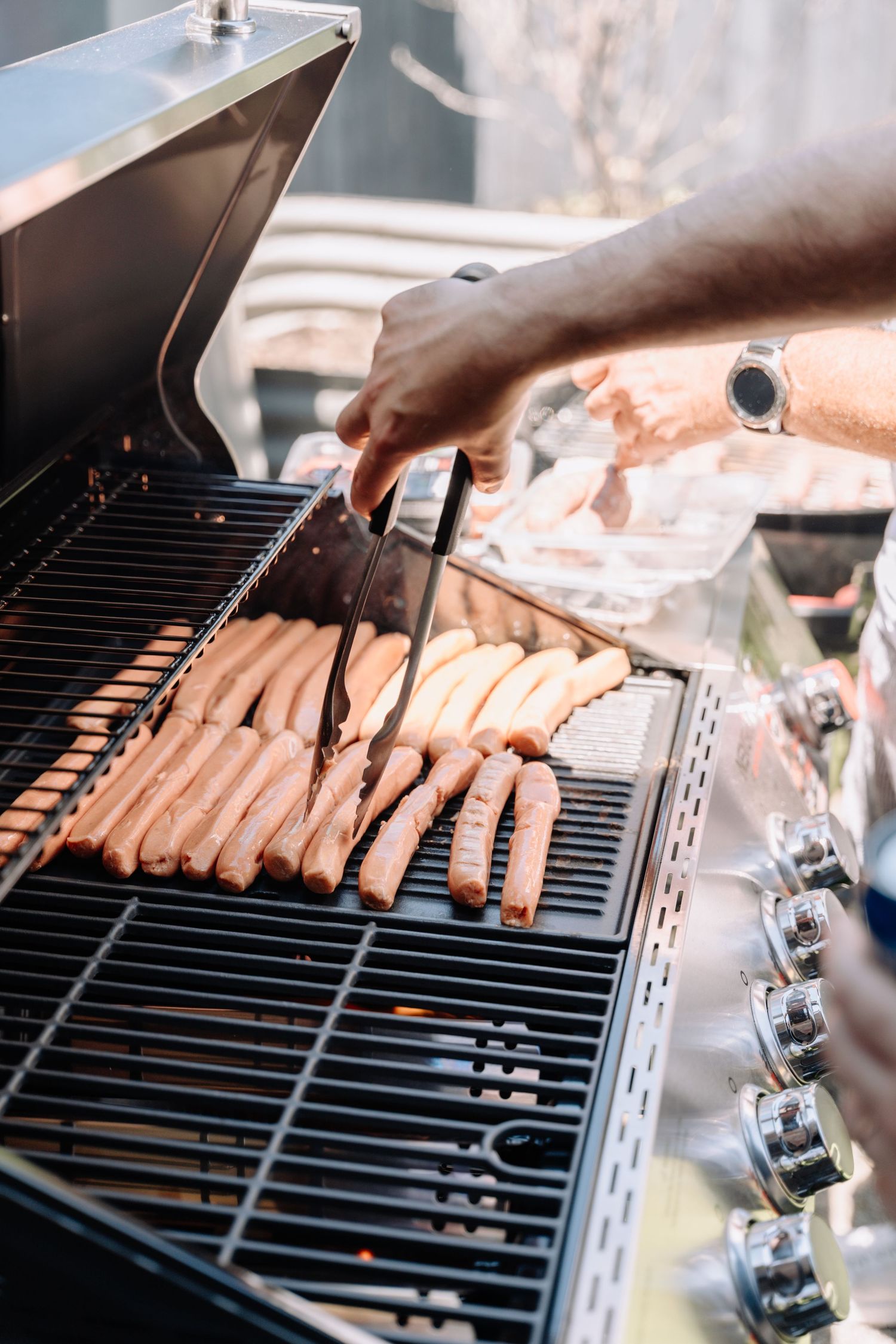 Hot dogs being grilled on black metal grates of a barbecue grill.