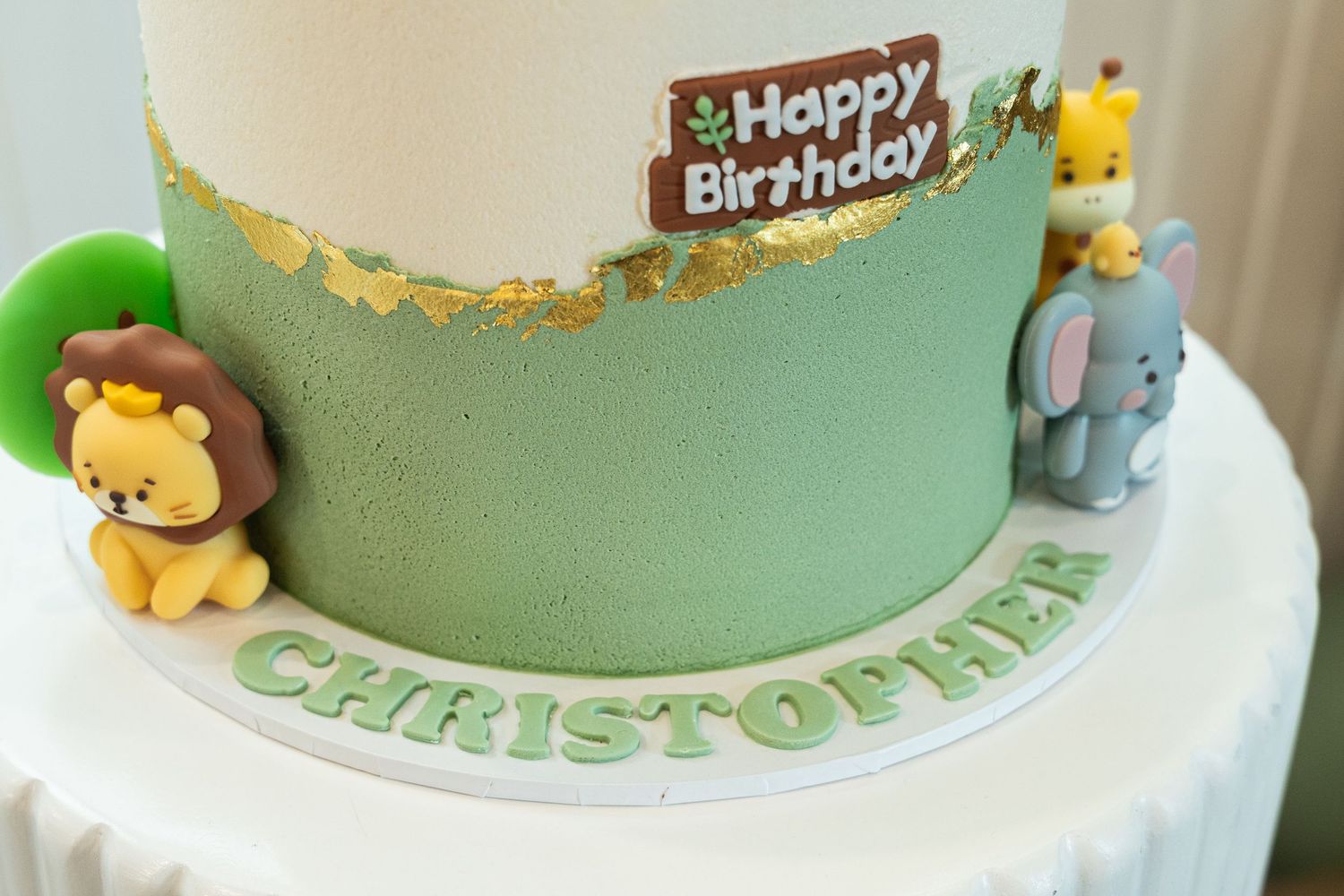 A green safari-themed birthday cake decorated with fondant animals and a brown birthday sign on top.