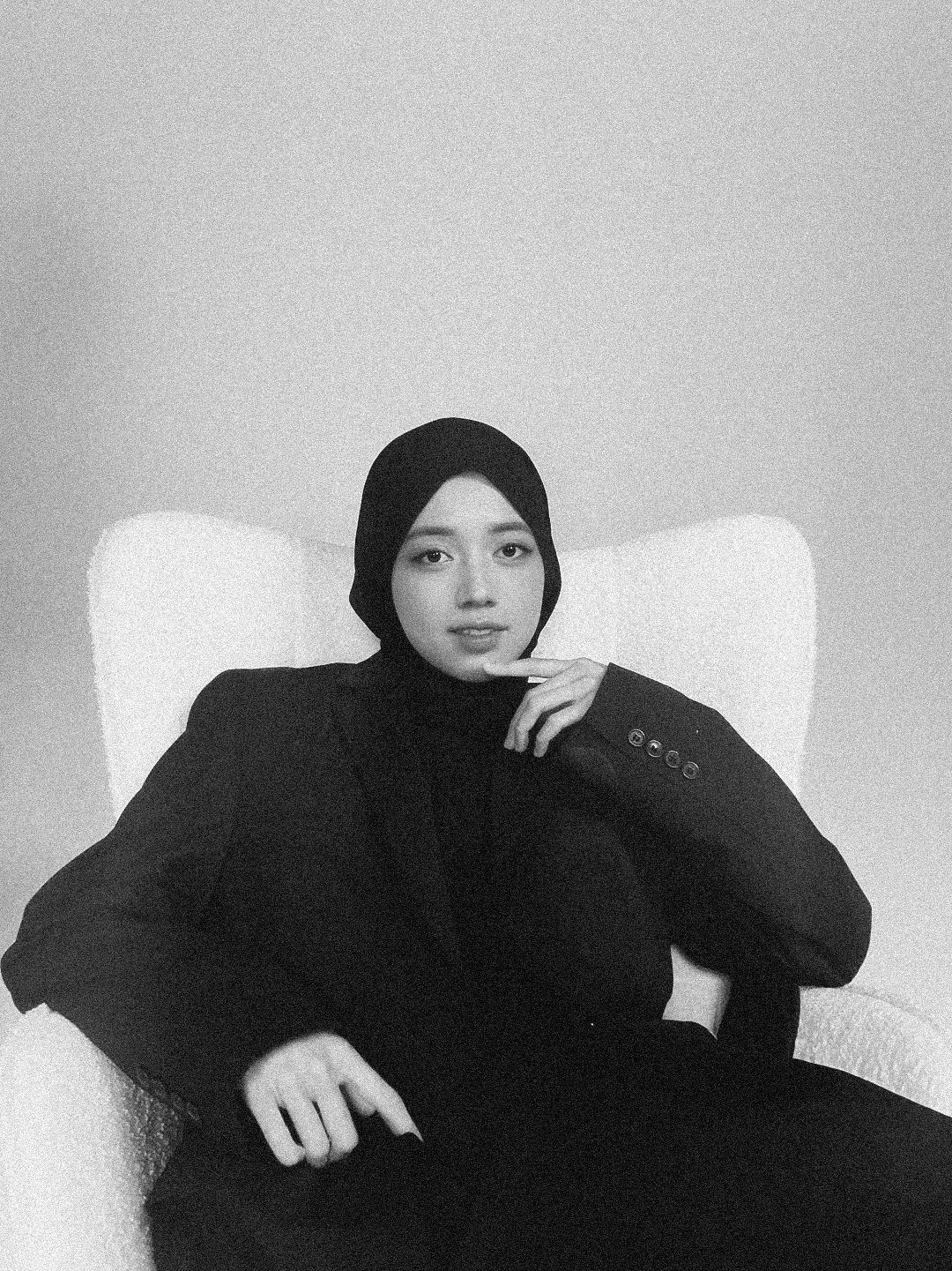 Elegant monochrome portraits of figure reclining on white chair in studio.