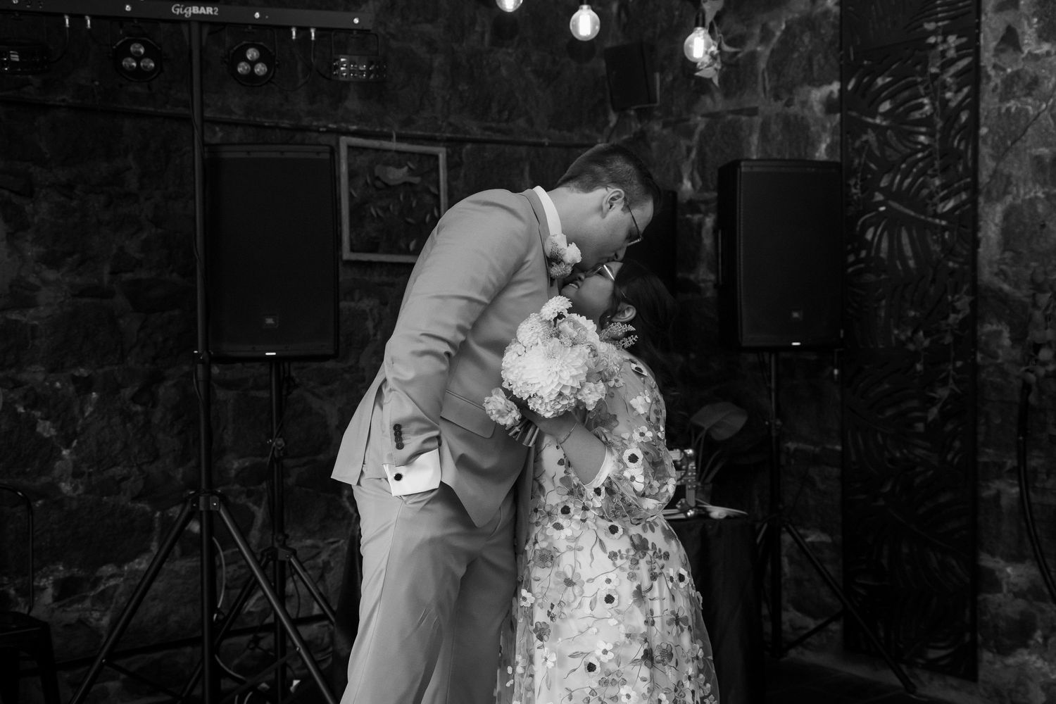 Black and white photo of couple sharing first kiss at wedding reception.