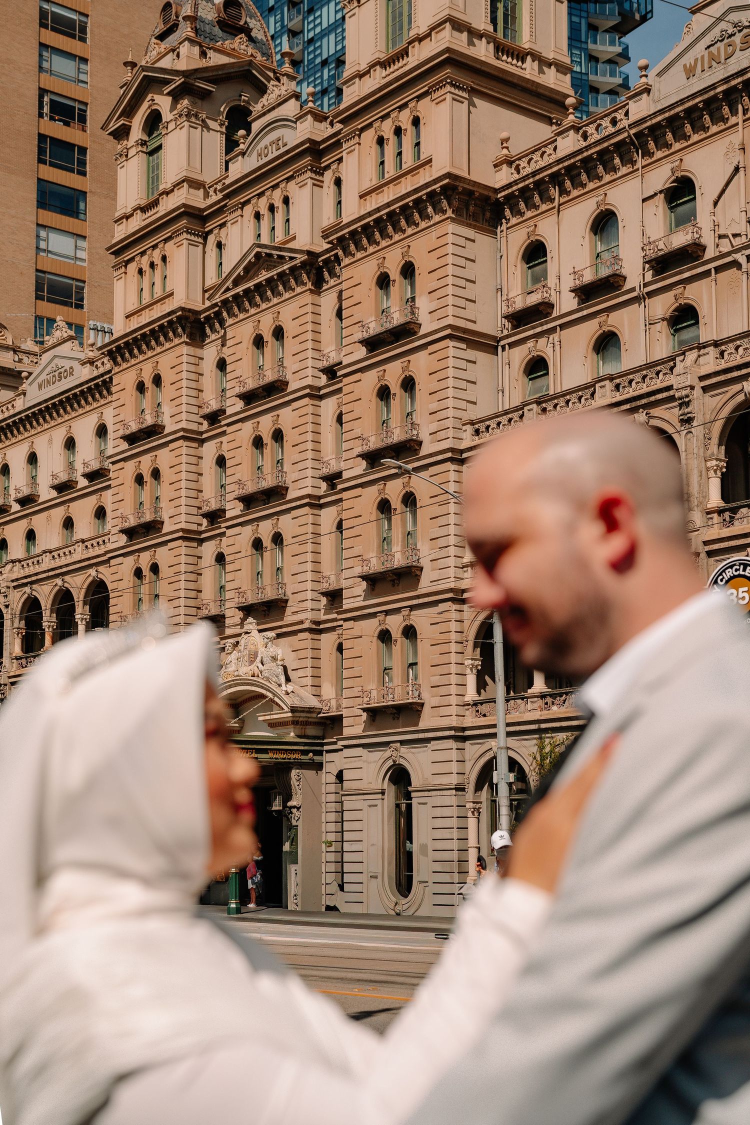 Bride and groom share romantic moment in front of grand historic sandstone building on their wedding day.