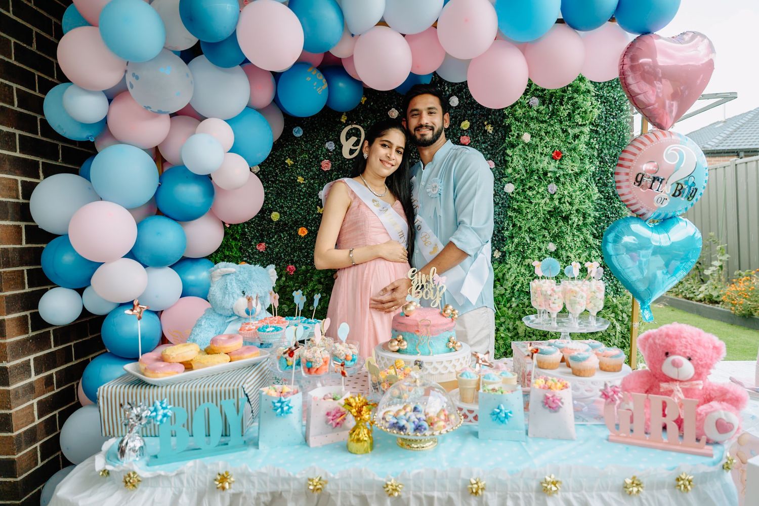 Pink and blue balloon arch decorates a festive party setup with dessert table and outdoor backdrop.