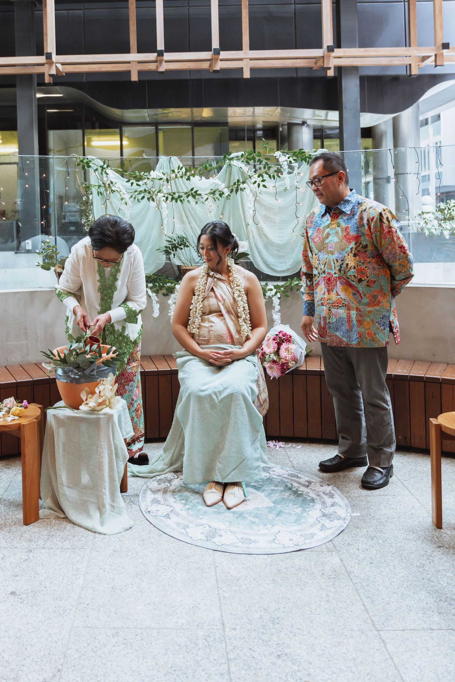 Traditional wedding ceremony setup with floral decorations and white backdrop in an indoor venue.