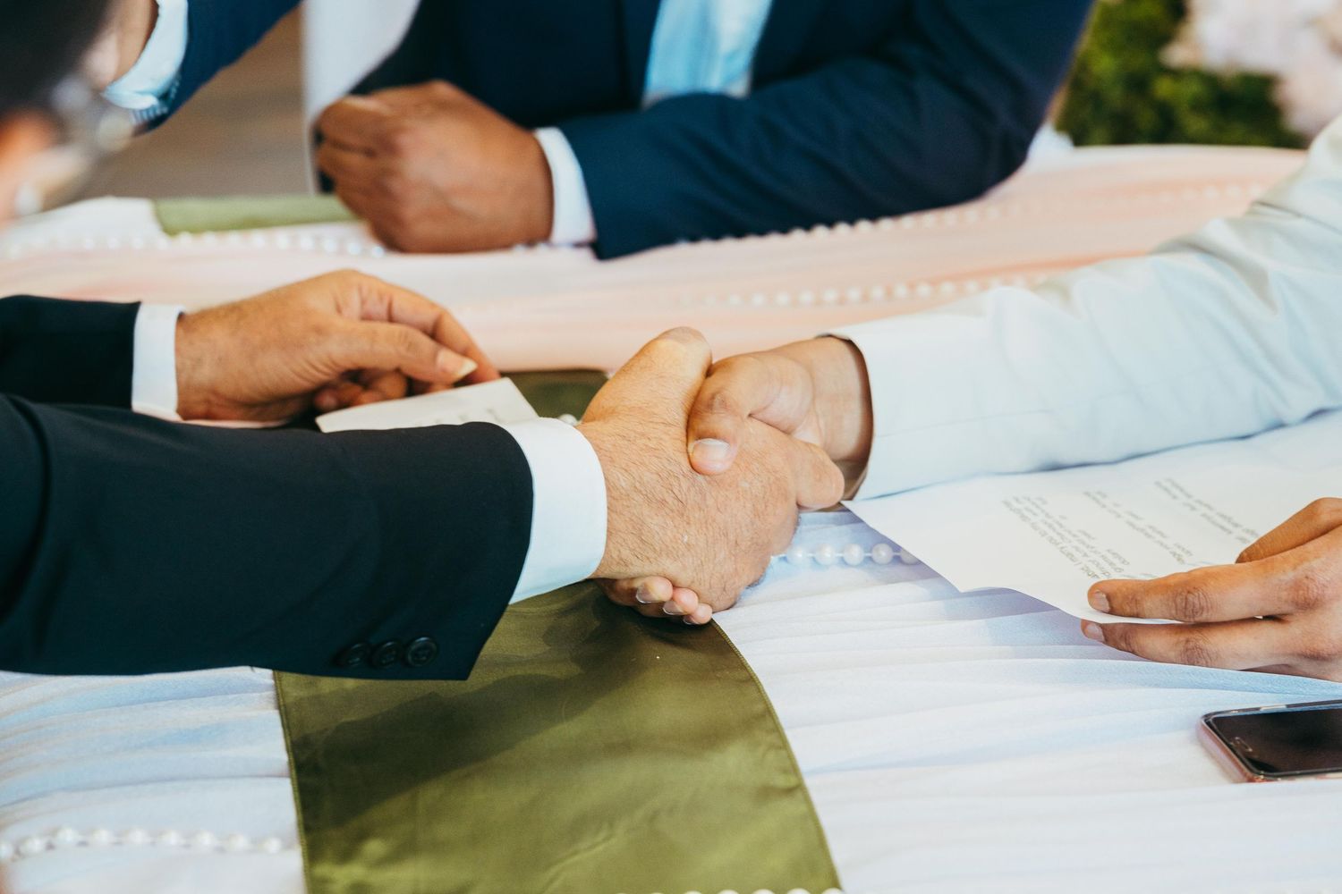 Groom and officiant shake hands over wedding documents during signing ceremony.