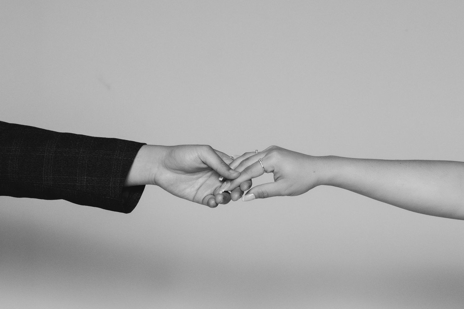 Black and white photo of two hands gently touching fingertips against a light gray background.