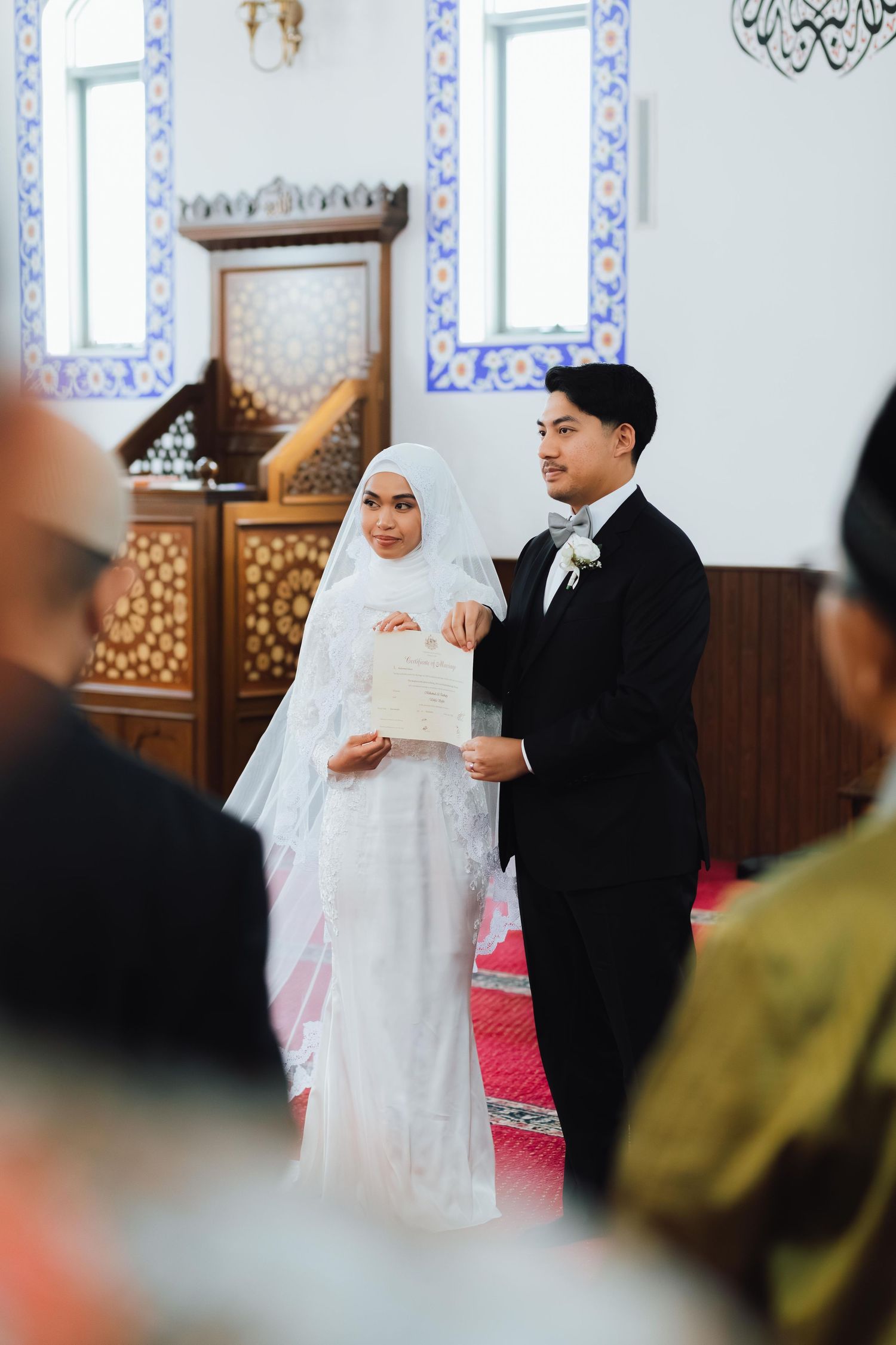 Muslim bride and groom holding marriage certificate during Islamic wedding ceremony in decorated mosque.