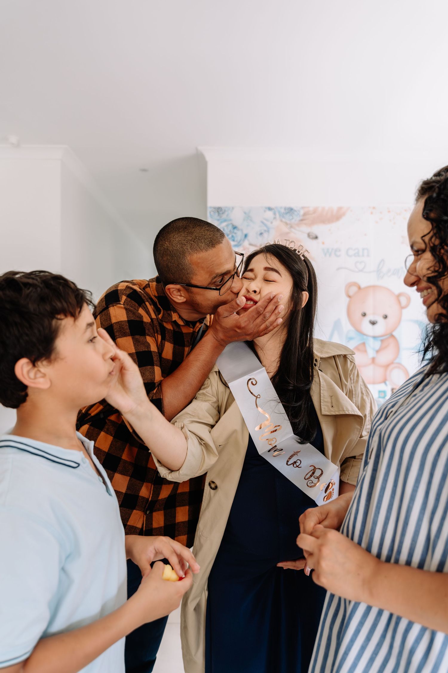 A playful family moment shows loved ones sharing laughter and affection in front of a wall with teddy bear decorations.