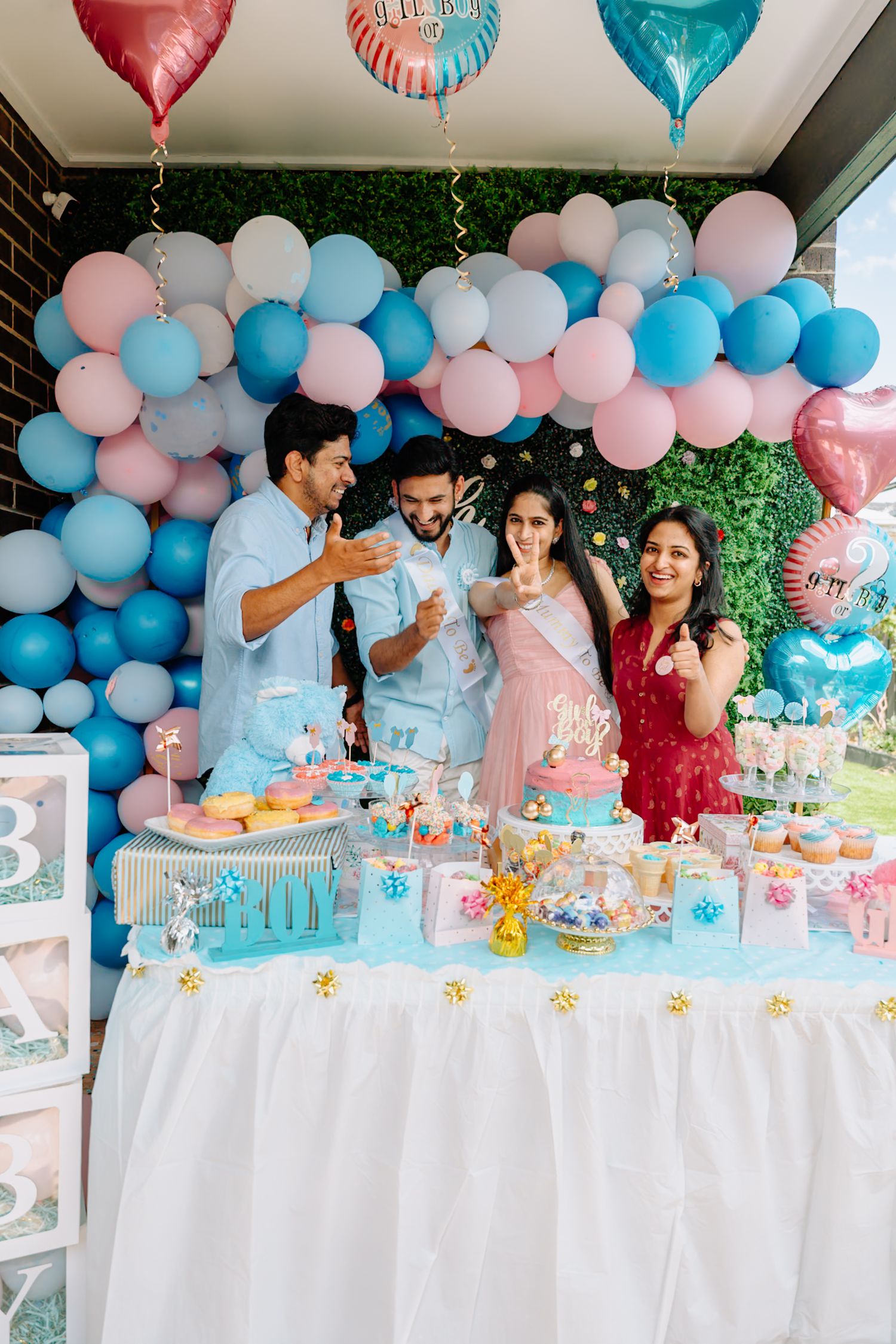 Gender reveal party setup with blue and pink balloon decorations and white dessert table.