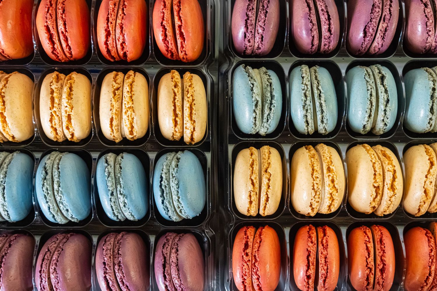 Colorful French macarons arranged in neat rows displaying vibrant pastel shades of pink, blue, orange and purple.