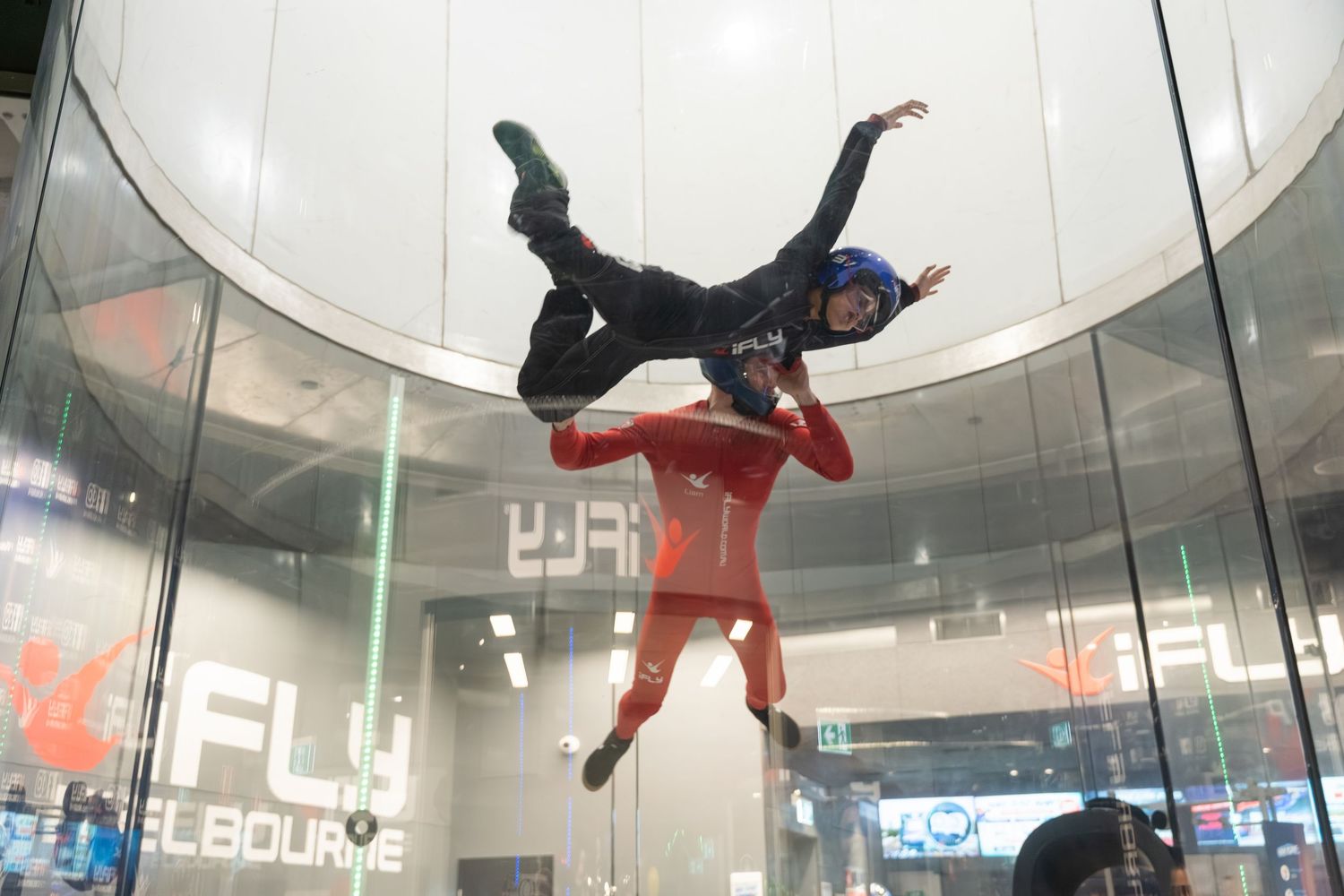 Indoor skydiving participants float in vertical wind tunnel while practicing aerial maneuvers in a training facility.