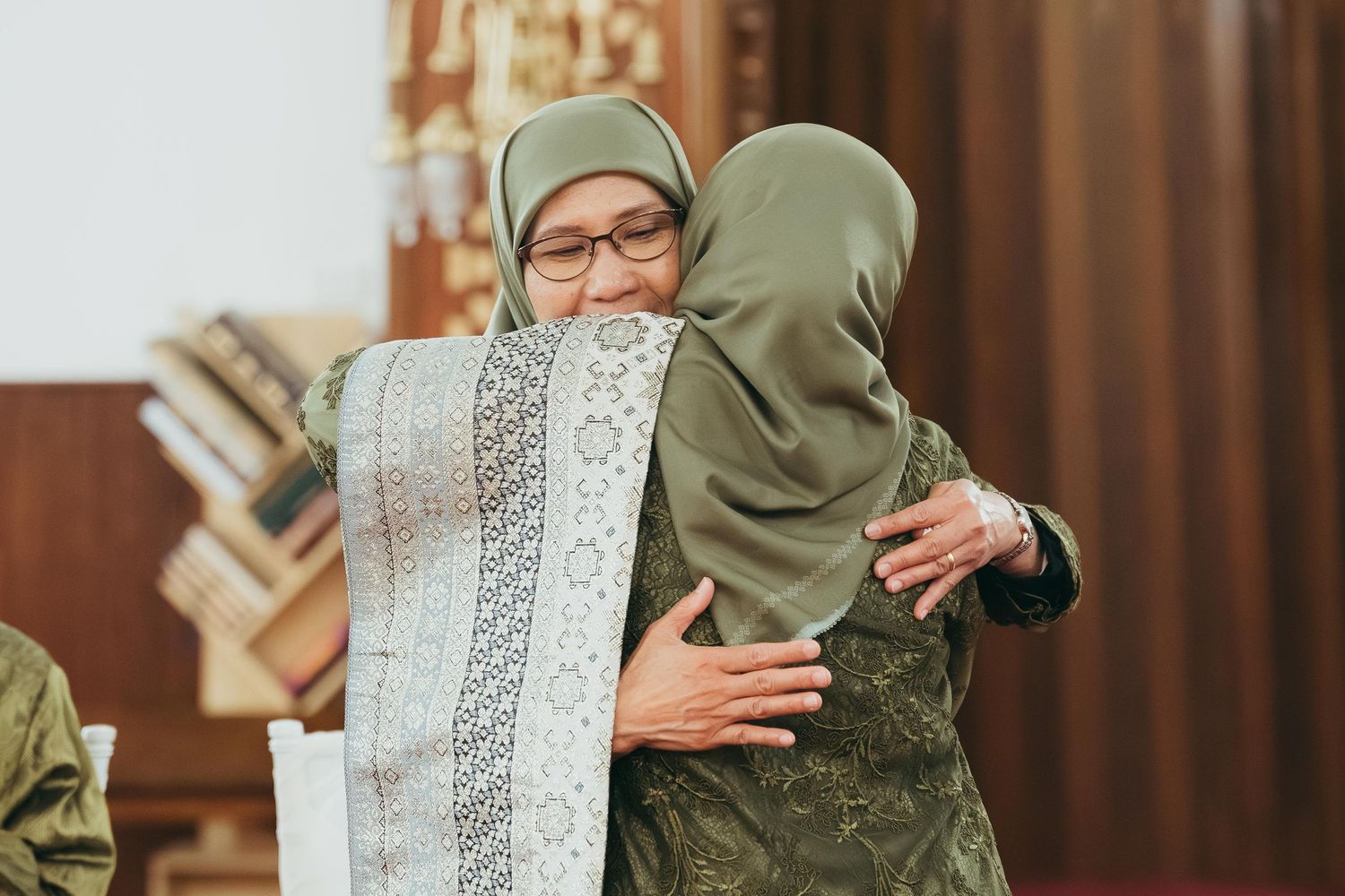Two women in hijabs share a warm embrace during a Muslim wedding celebration.