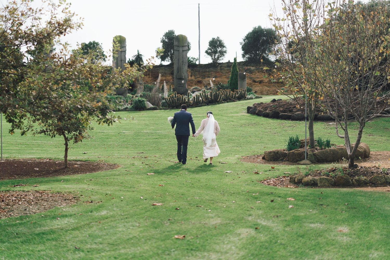 Bride and groom walking hand in hand through a lush green garden venue on their wedding day.