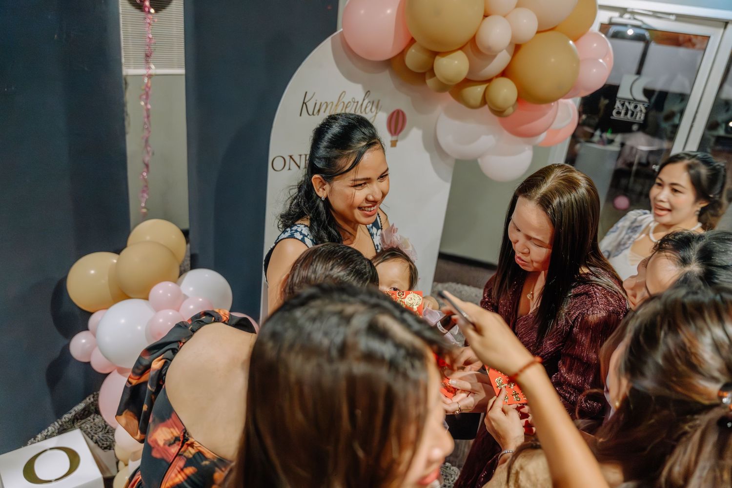 Group of guests gathered around a balloon arch at a festive indoor celebration.