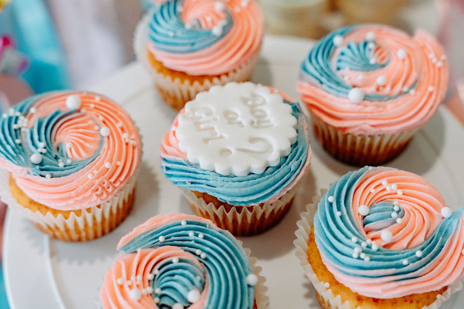 Homemade cupcakes decorated with swirled pink and blue frosting in a two-tone pattern on a white surface.