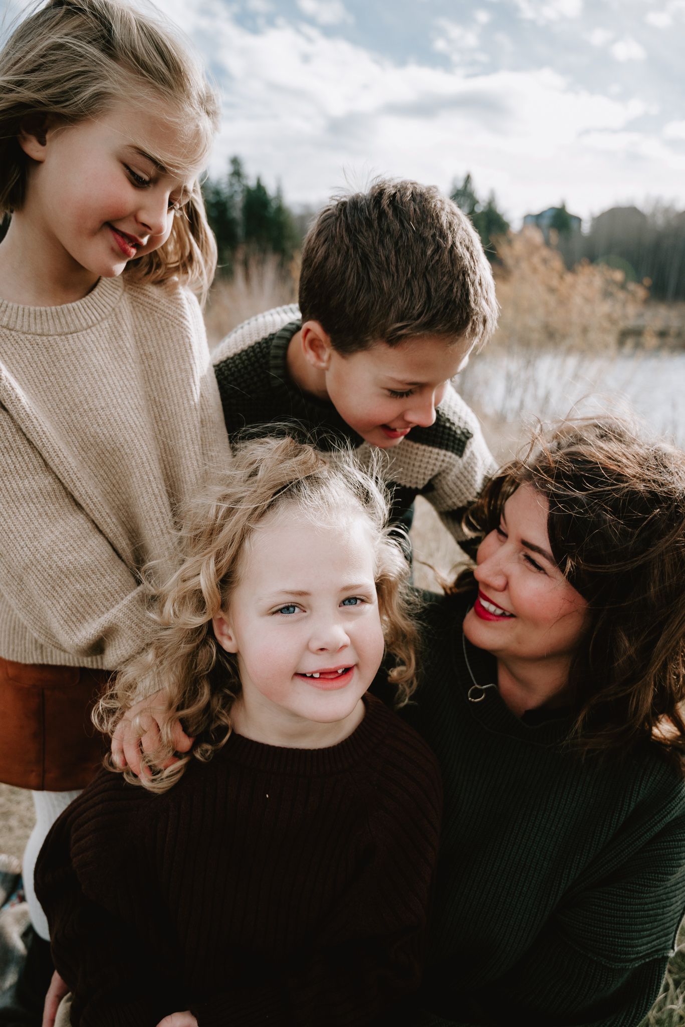 A joyful family portrait of a mother with three children smiling outdoors near a lake in autumn.