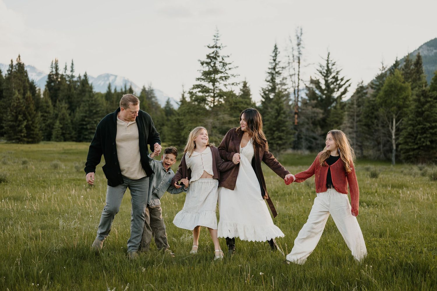 Family of five walking hand in hand through a green mountain meadow in Banff.