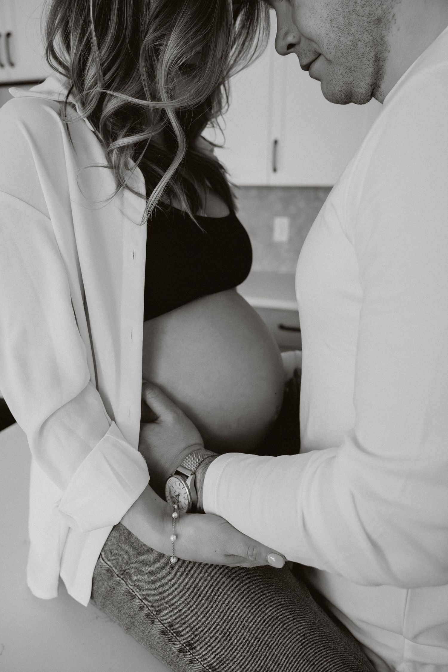Black and white photo of a couple holding hands while the man gazes at her pregnant belly.
