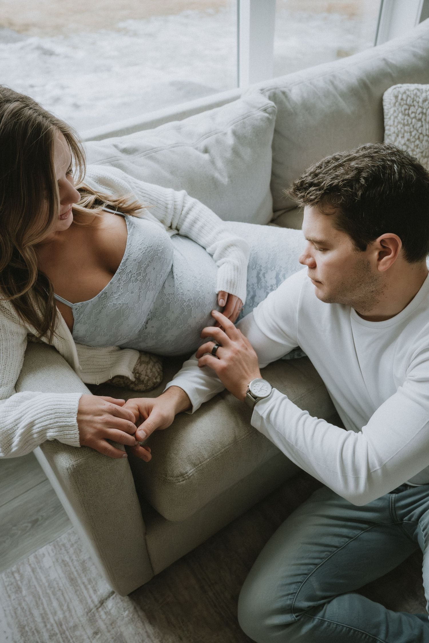 Couple sharing a tender moment at home, pregnant woman resting on couch while partner sits beside her.