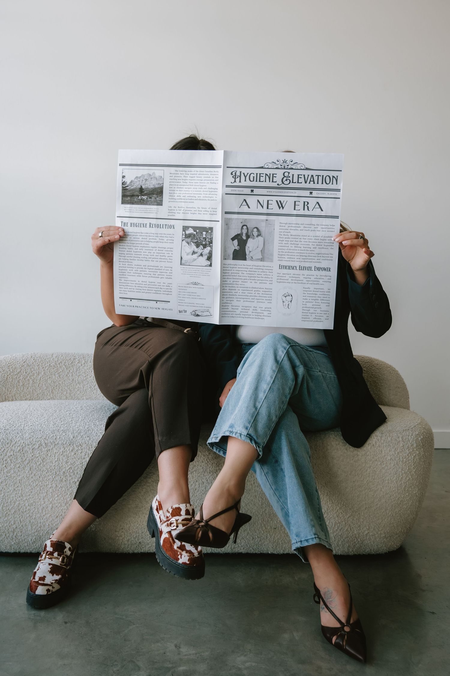 Two people sitting on sofa hiding faces behind Hygiene Elevation newspaper, wearing stylish shoes.