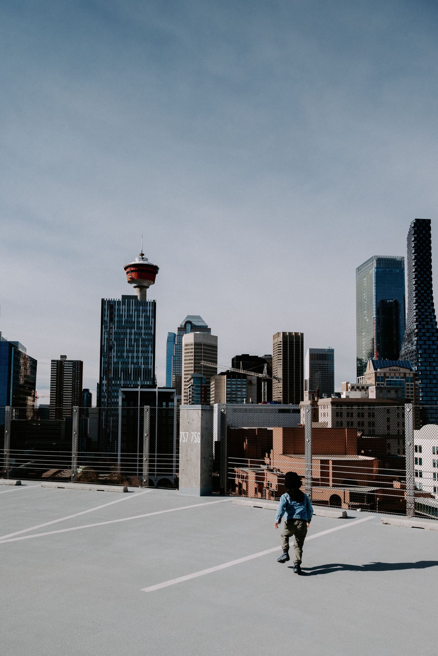 A child walks alone on a rooftop parking lot with Calgary's downtown skyline in the background.