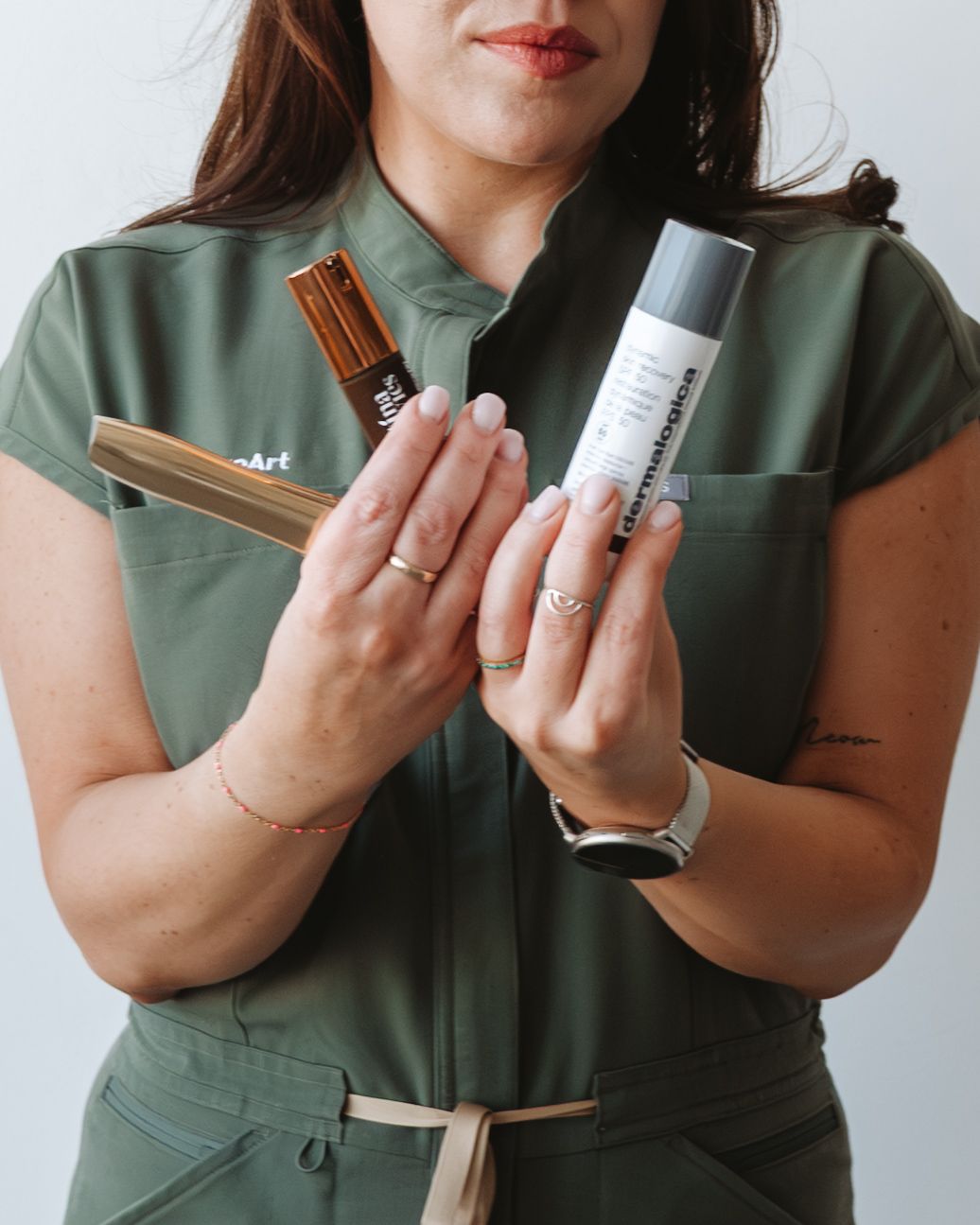 Woman in green jumpsuit holding skincare products, showcasing beauty and wellness items in a professional setting.