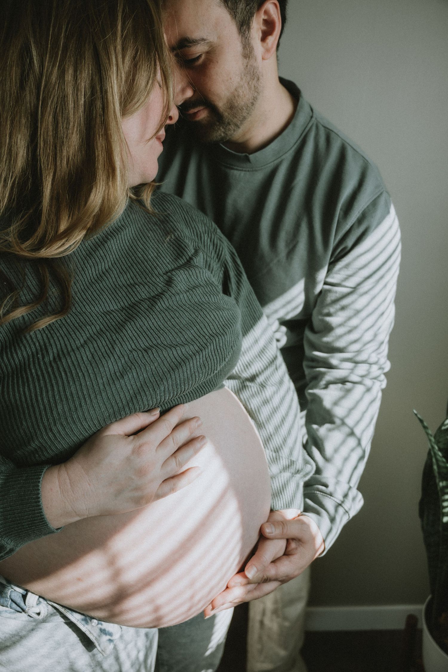 Couple sharing tender moment, man embracing pregnant woman while holding baby bump.