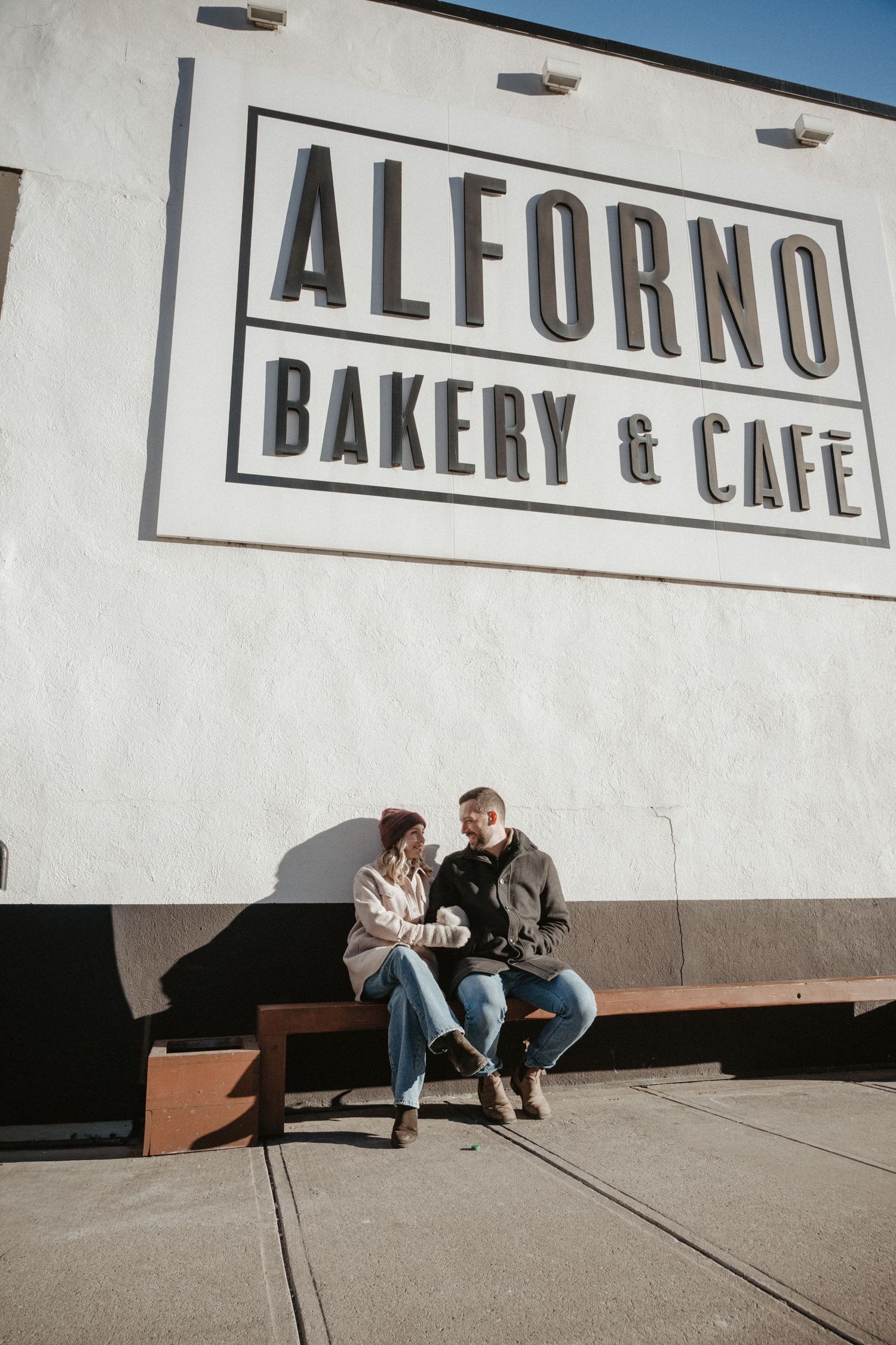 Couple sitting on a bench outside Alforno Bakery & Cafe, sharing a warm moment on a sunny day.