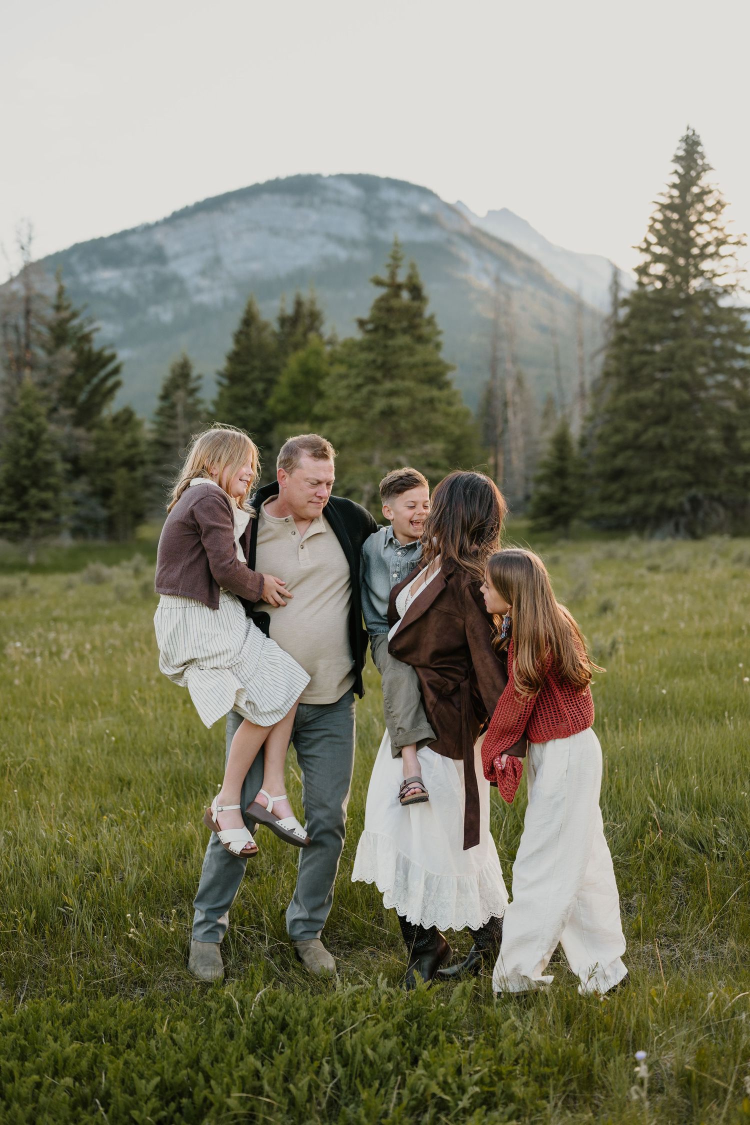 Joyful family of five playing together in a scenic mountain meadow in Banff.