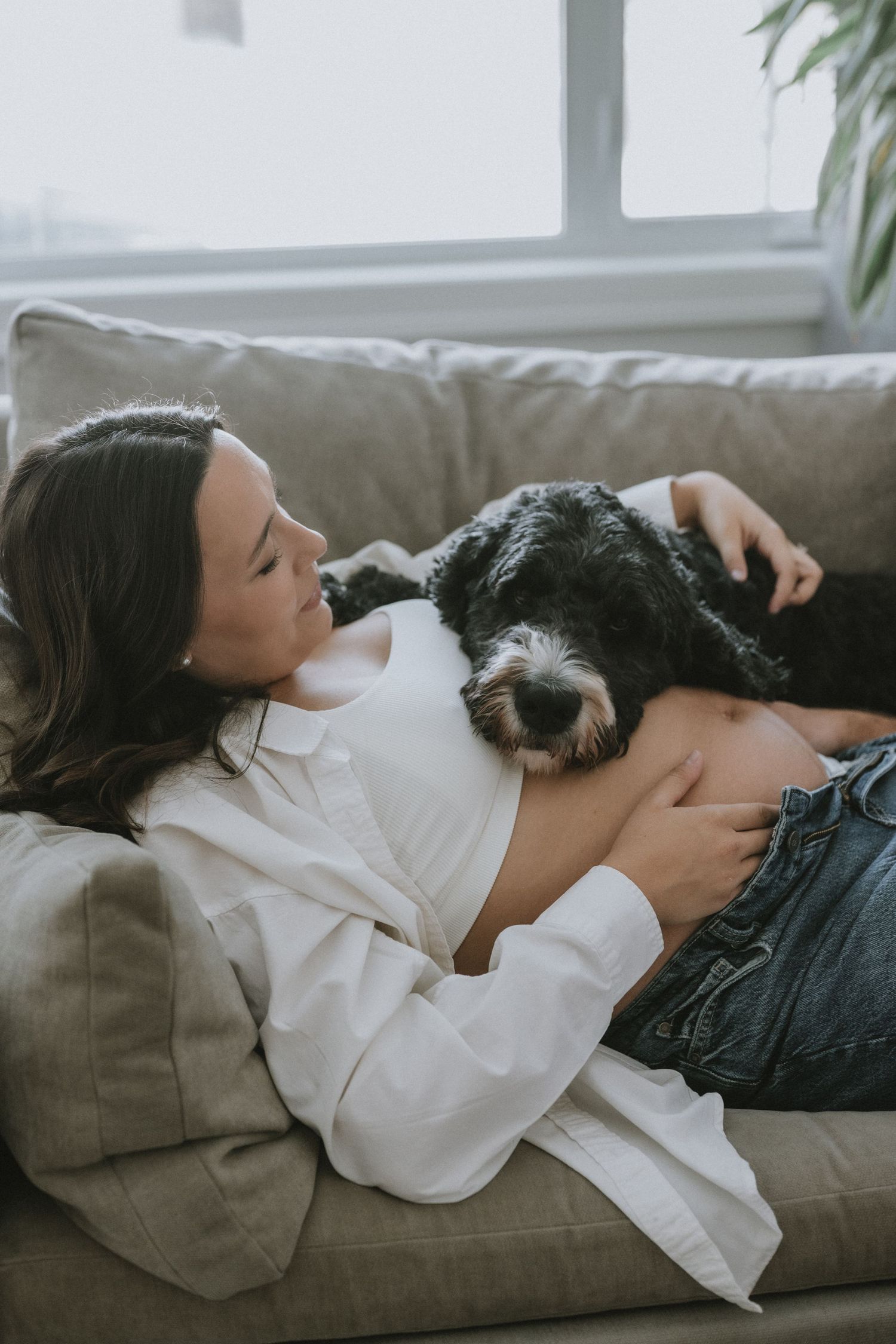 Woman relaxing on couch cuddling with black and white dog, enjoying a cozy moment at home.