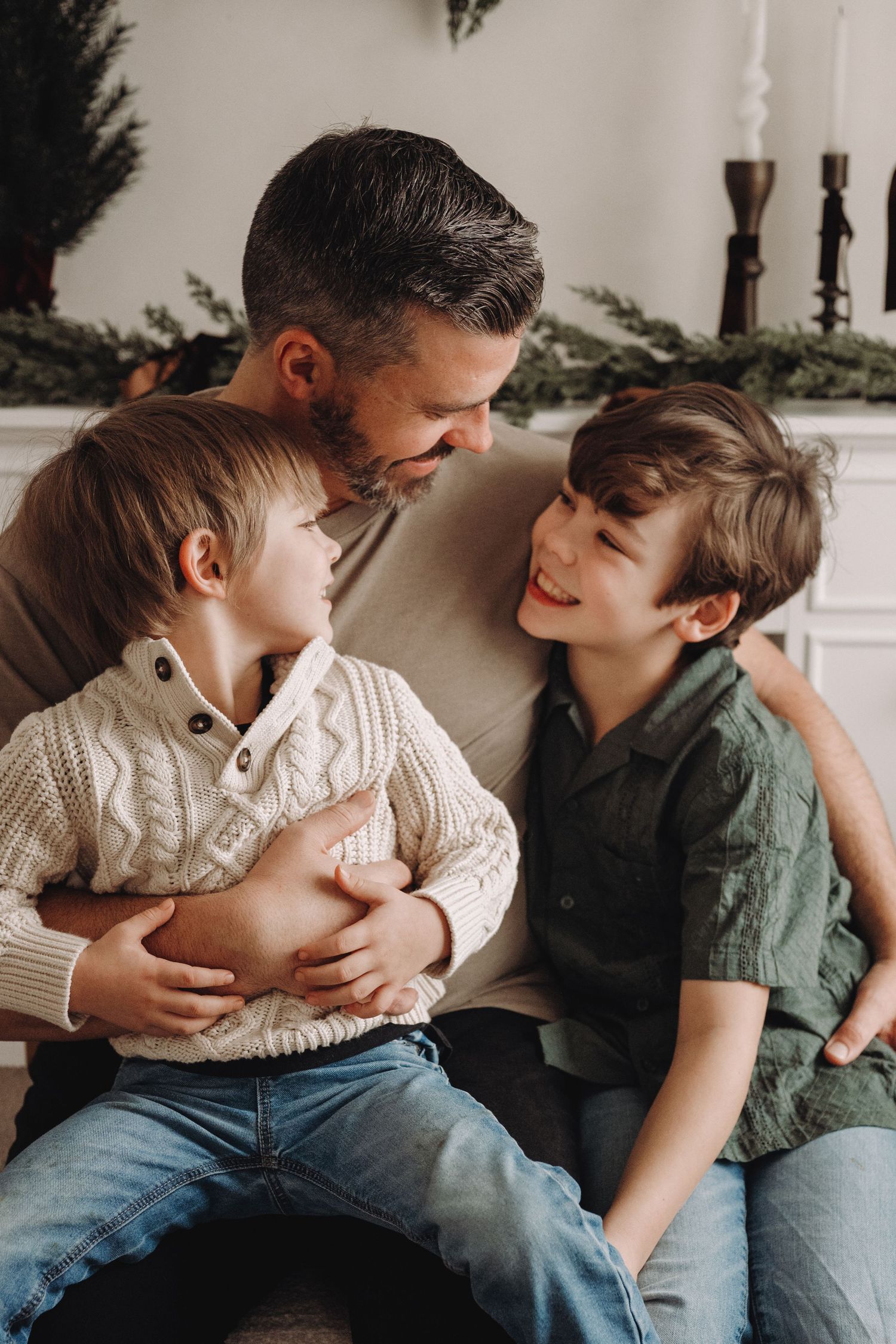 A father smiles warmly at his two young sons during a cozy Christmas family portrait session.