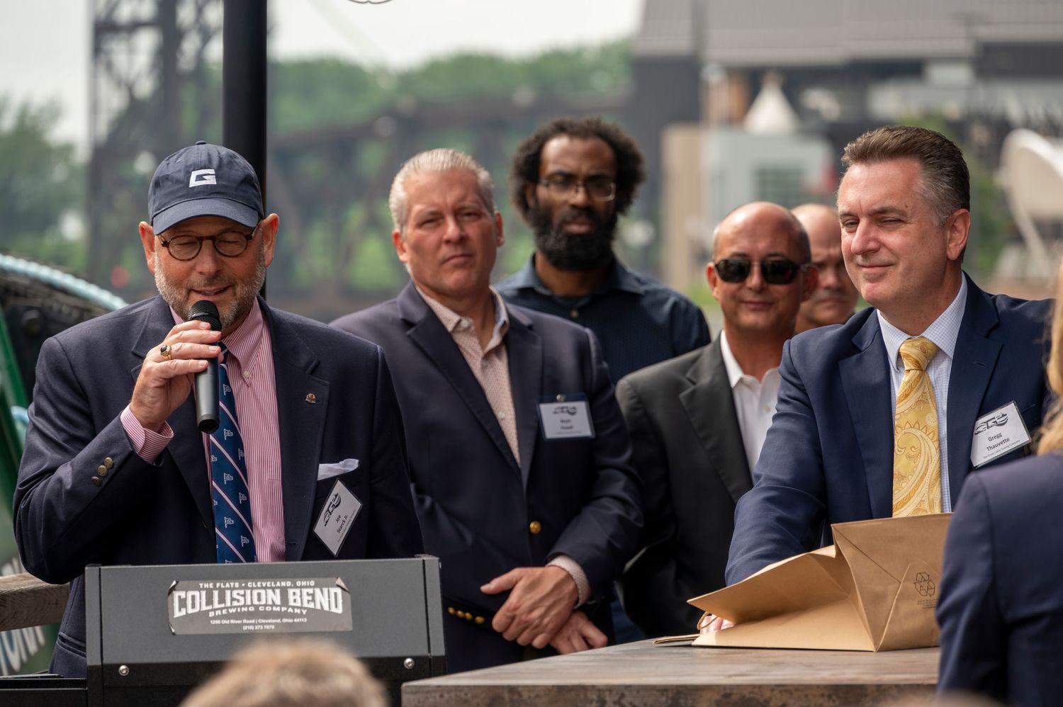 Two men speaking at podium during outdoor event at Collision Bend venue.