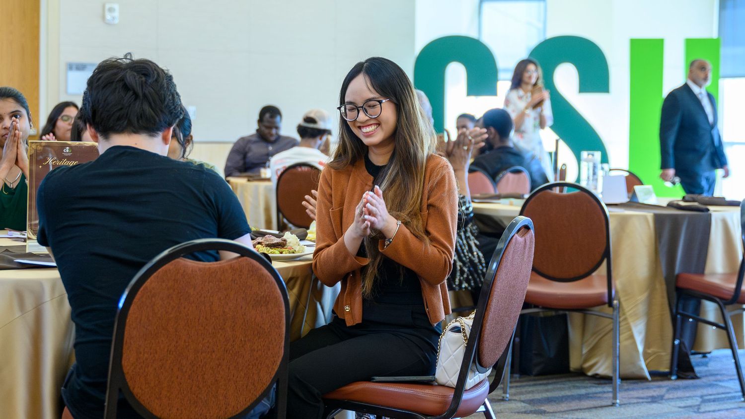 Students networking at a CSU campus event, seated at round tables in a modern conference hall.