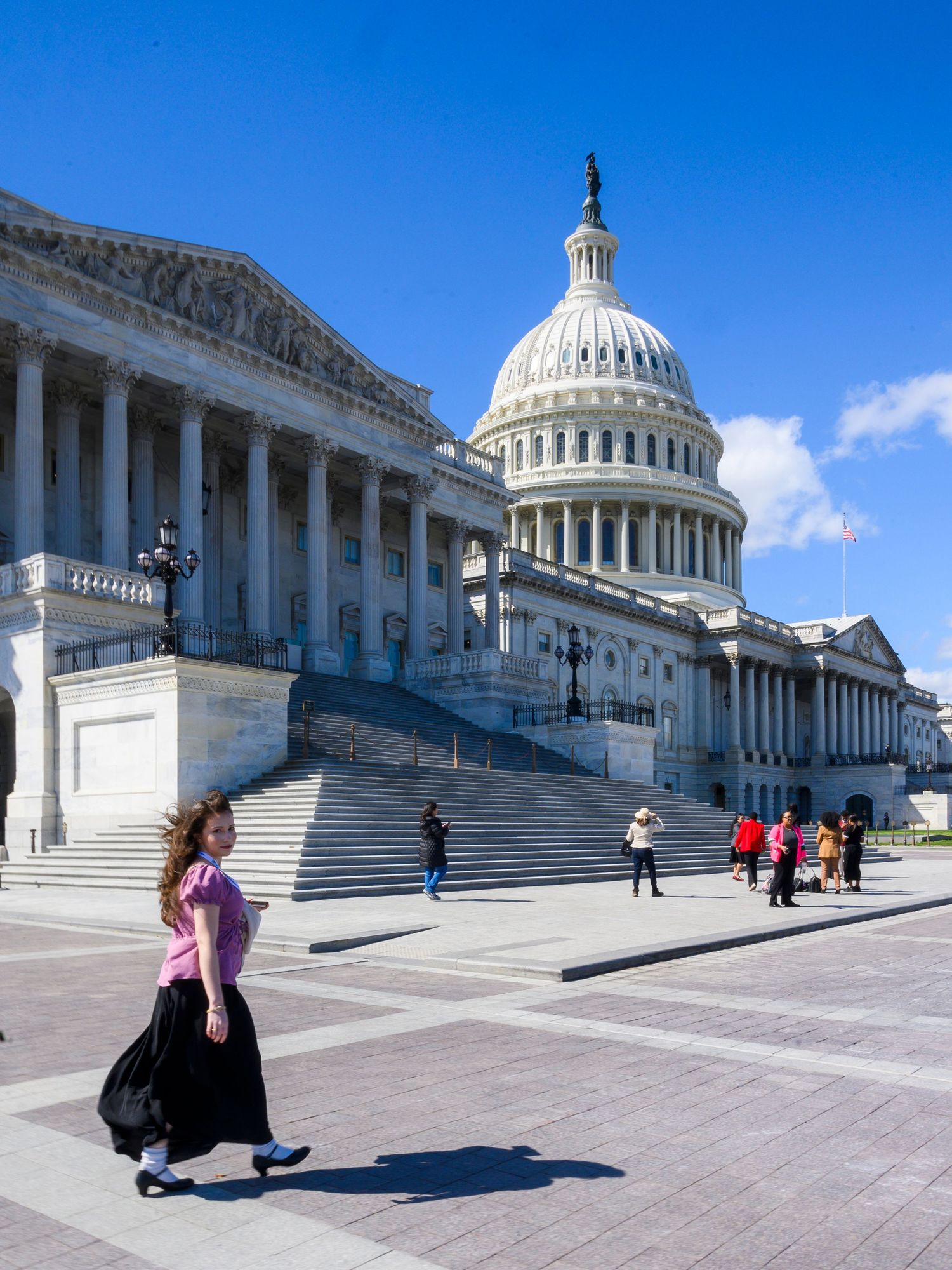 Woman in pink top walking past the US Capitol building on a sunny day in Washington DC.