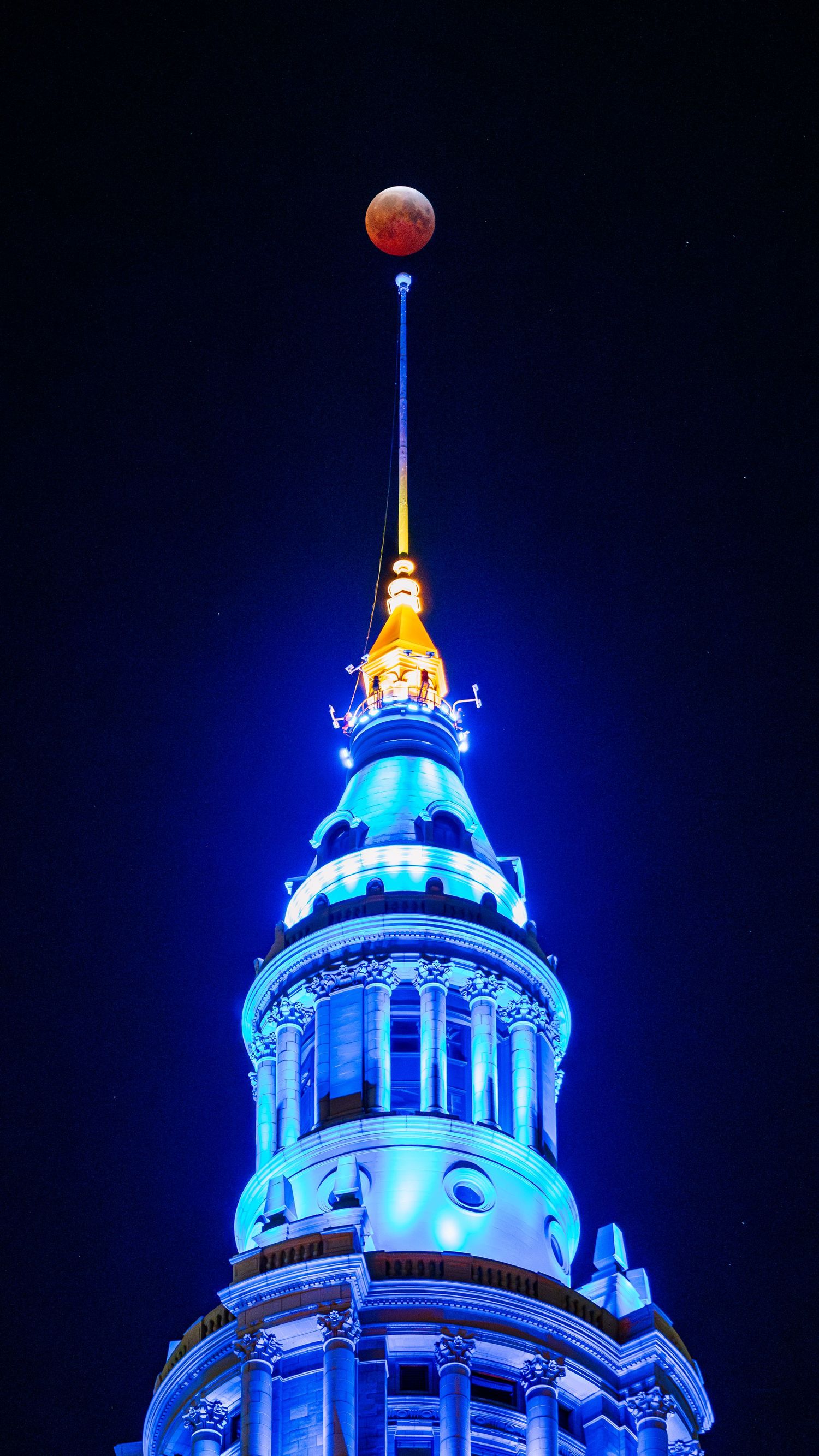 Cleveland Terminal Tower glowing blue and gold at night with a blood moon lunar eclipse above the spire.